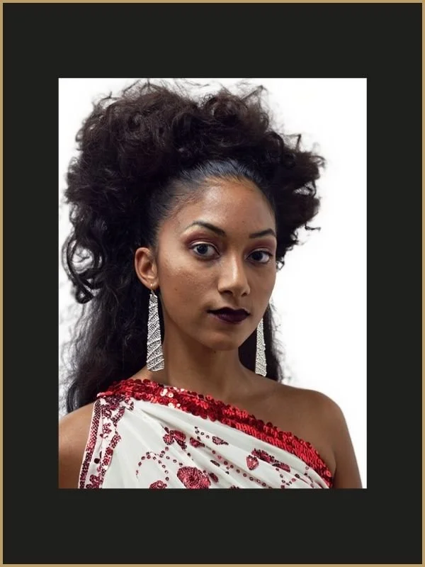 Jeune femme tressée avec de longues boucles noires, portant de longues boucles d'oreilles et une robe blanche avec des détails rouges