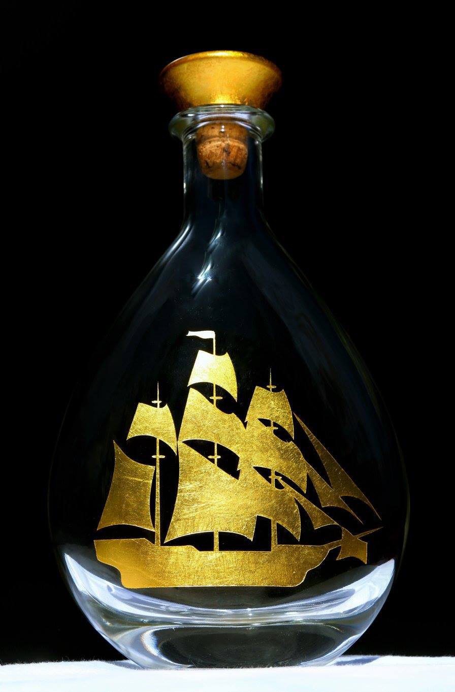 Bouteille en verre transparent avec gravure d'un bateau à voiles en or.