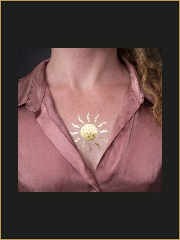 Peau nue avec tatouage d'un soleil doré sur le décolleté, portant une chemise rose en satin.