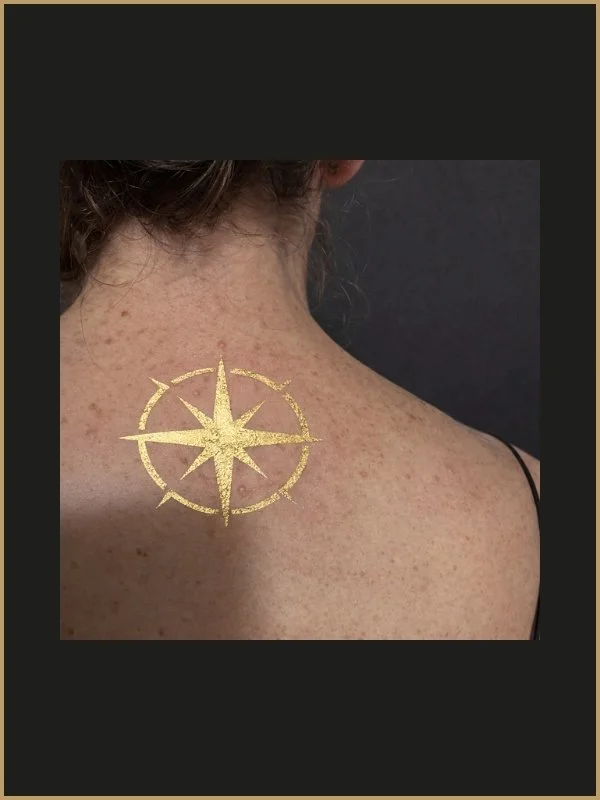 Tatouage doré d'une boussole sur le haut du dos d'une femme.