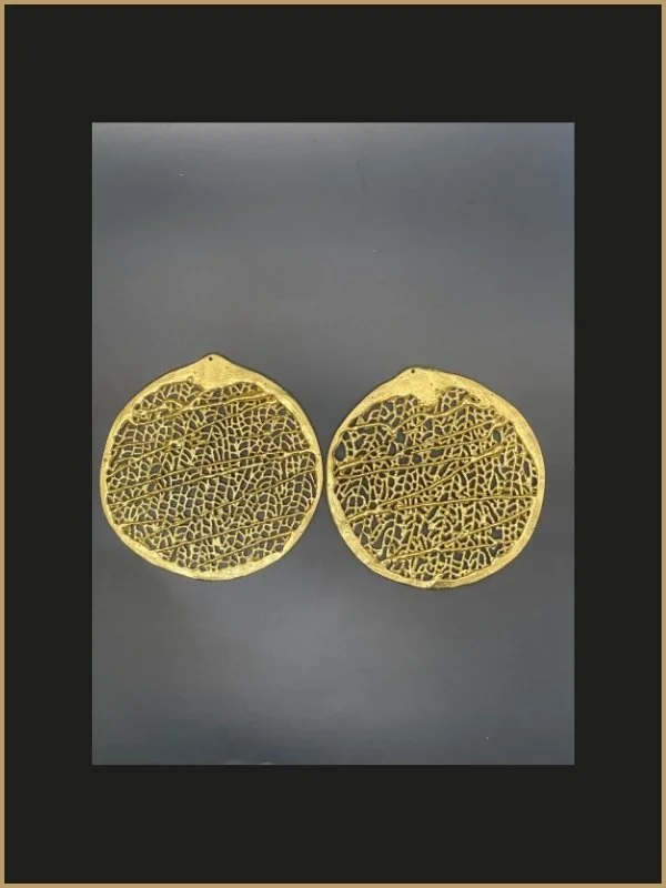 Boucles d'oreilles dorées avec un design intricate et rétro, rondes, sur un fond gris.