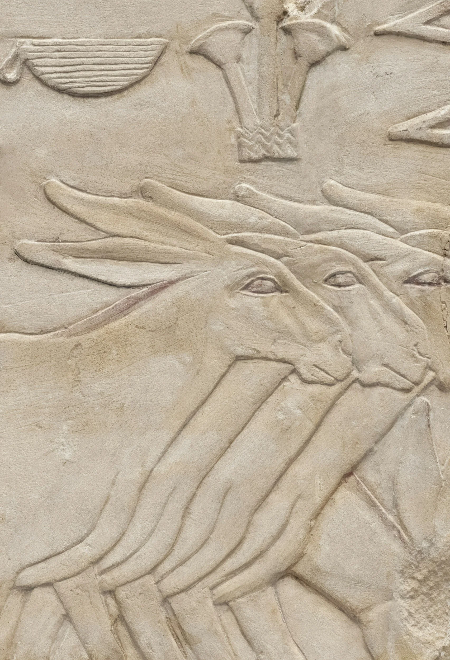 Ancient Egyptian-style carved relief featuring a stylized animal, resembling a hybrid of a lion and a dog, with elongated features and detailed lines. The relief also shows additional hieroglyphic symbols above the animal.