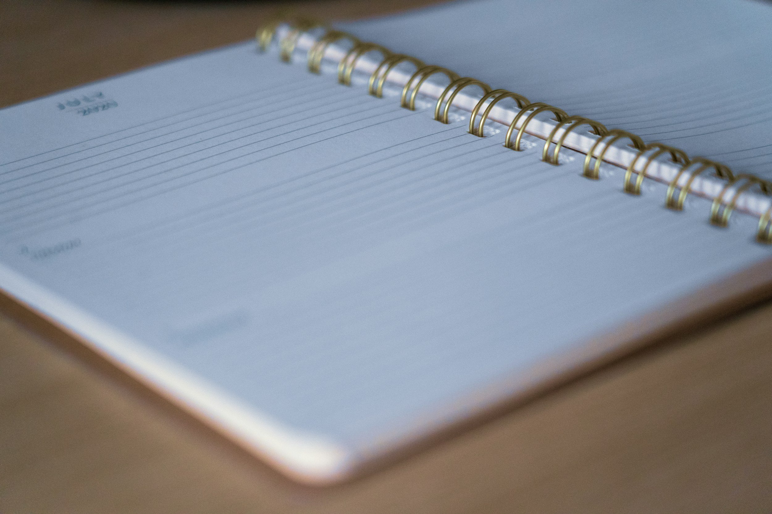 Open lined spiral notebook with gold coil binding, placed on a wooden surface.