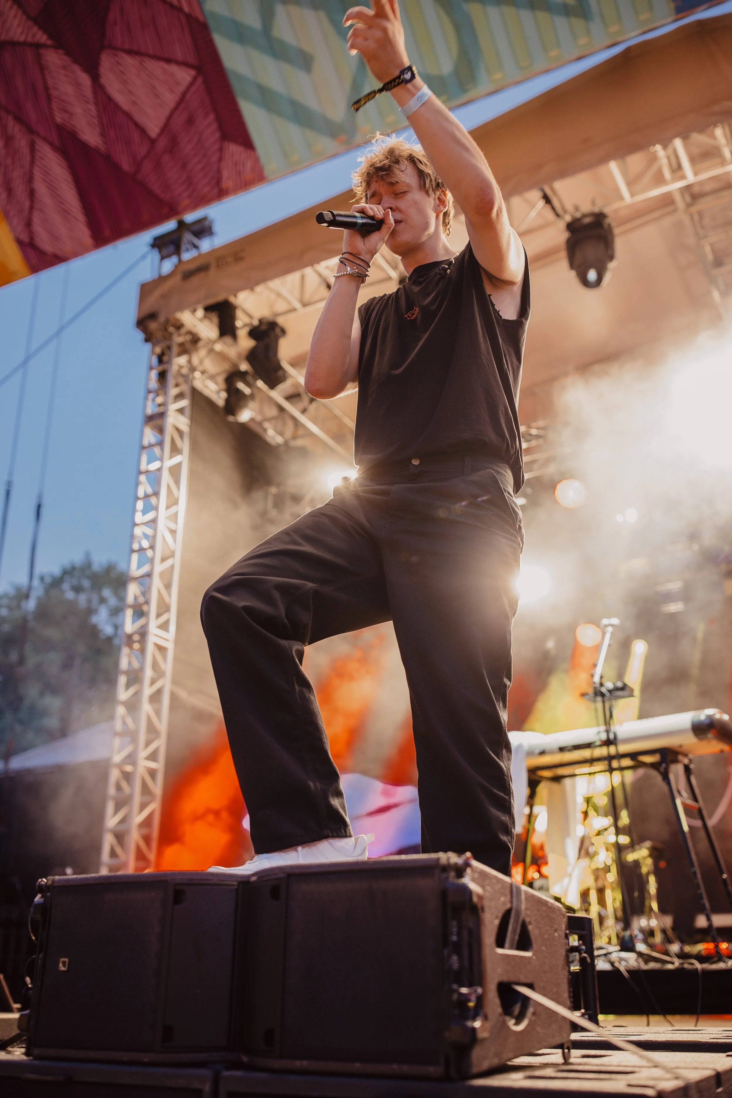 Junger Mann singt mit einem Mikrofon auf einer Bühne bei einem Konzert. Im Hintergrund sind Lichter und Rauch zu sehen.