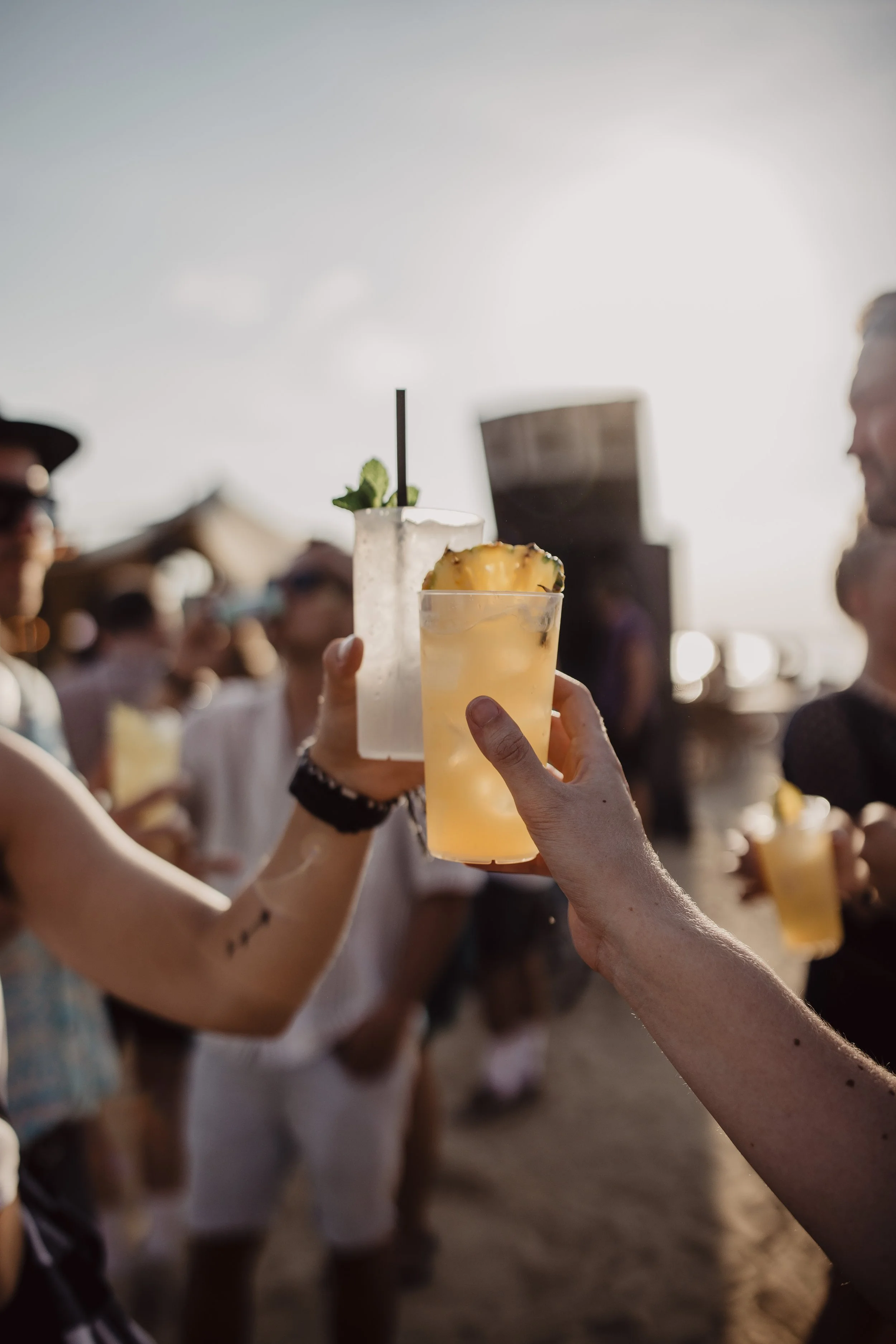 Menschen feiern am Strand und stoßen mit Cocktails an, bei Sonnenuntergang, im Freien.