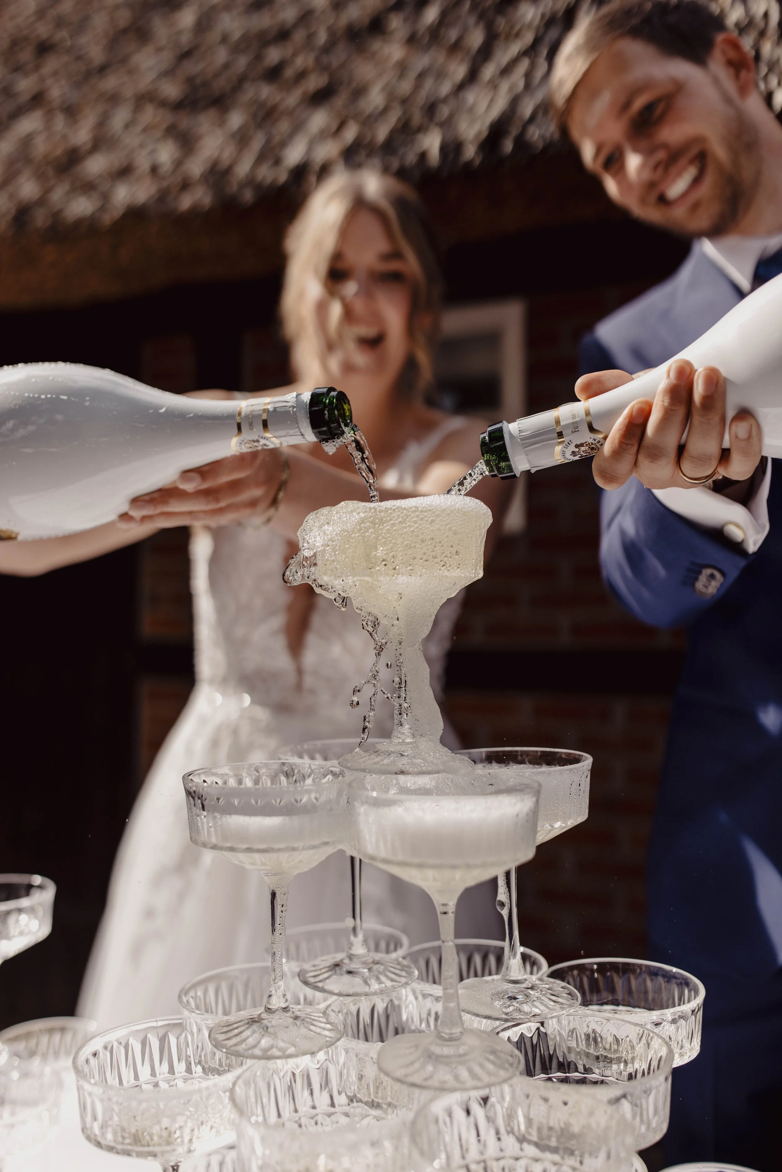 Hochzeitspaar beim Anstoßen mit Champagner, der auf einem Turm aus verbundenen Gläsern in der Luft besteht.