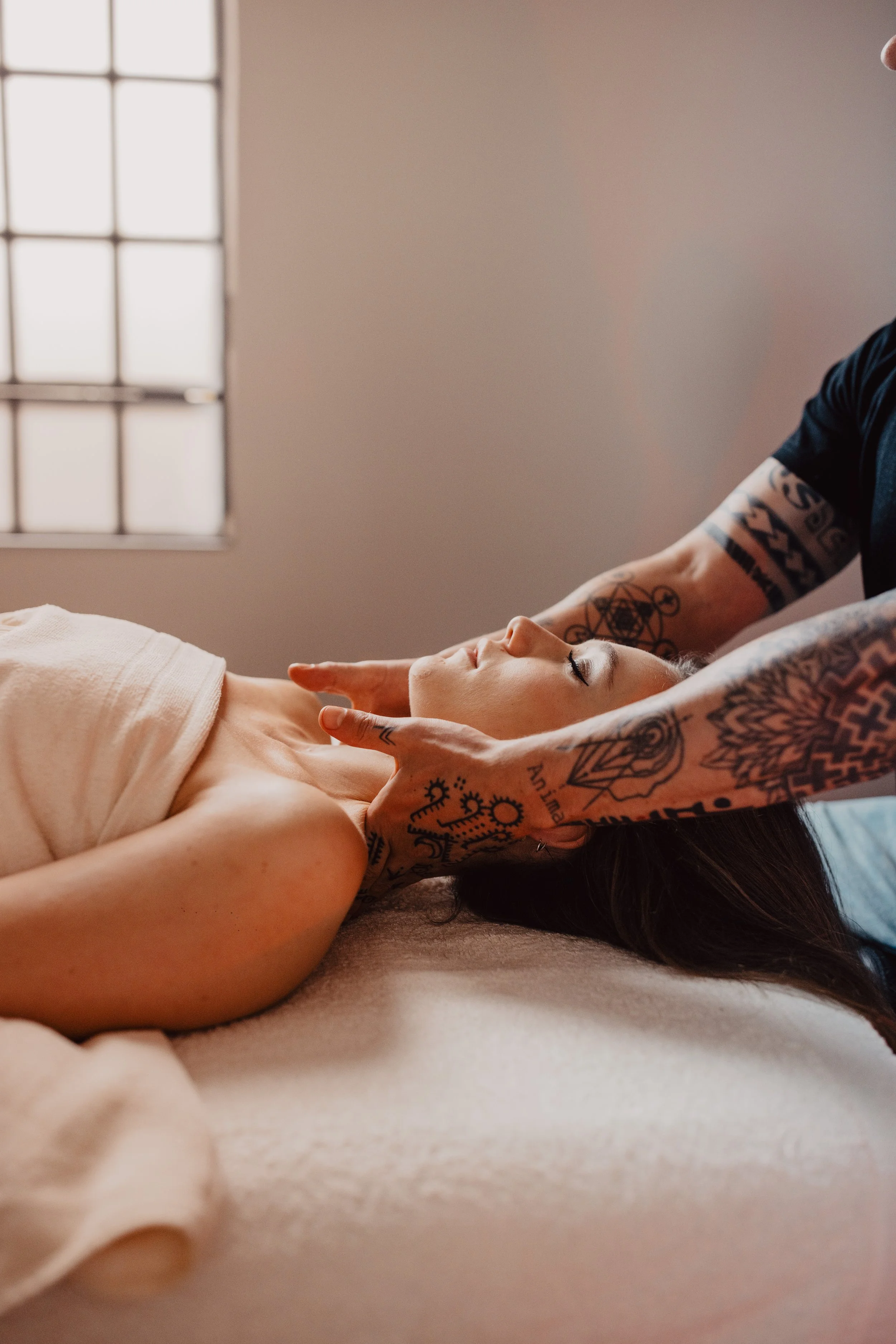 Eine Frau liegt entspannt mit geschlossenen Augen auf einer Massagebank, während eine massierende Person ihre Hals- und Kopfregion mit den Händen berührt.