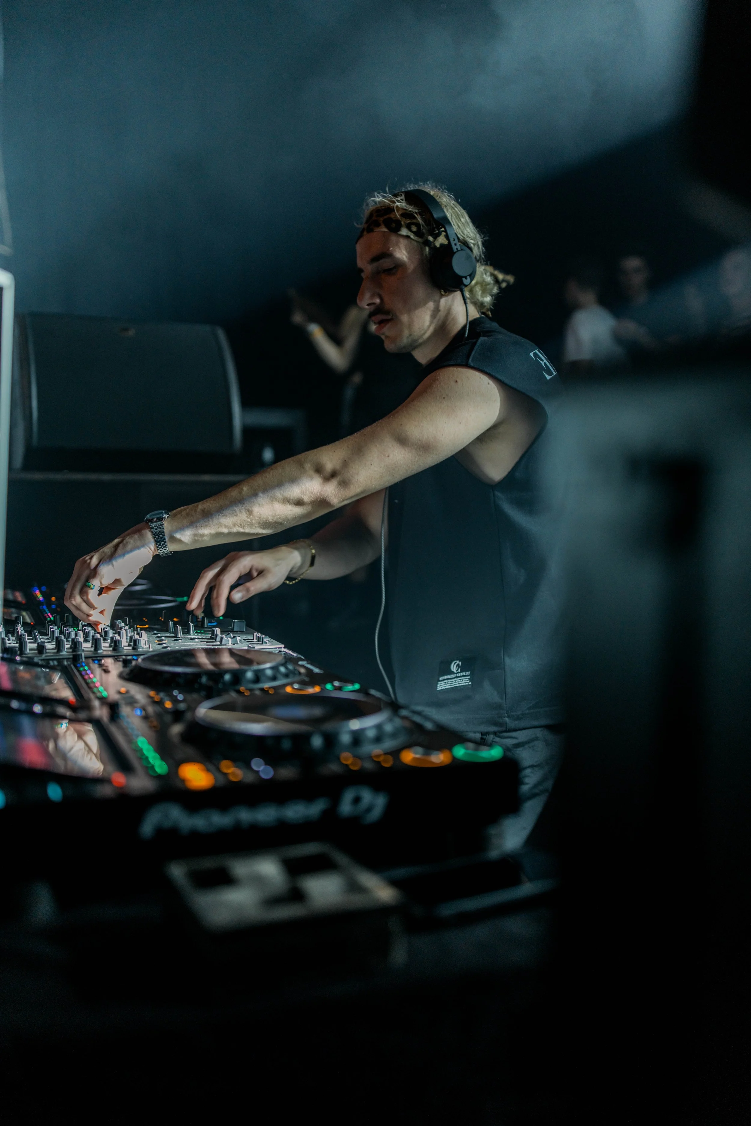 Ein DJ mit Kopfhörern, der an einem DJ-Controller in einem dunklen Club auflegt.