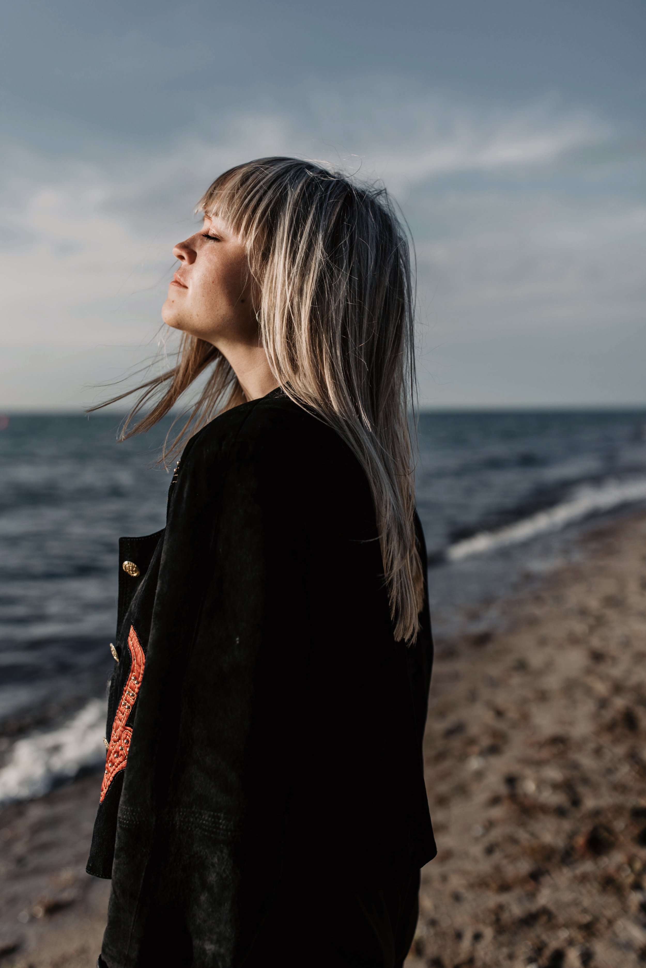 Frau mit geschlossenen Augen steht am Strand mit Blick auf das Meer bei Sonnenuntergang.