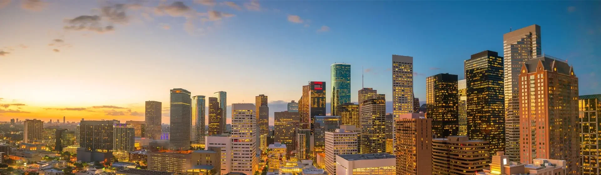 Skyline of downtown Los Angeles at sunset with illuminated skyscrapers and buildings.