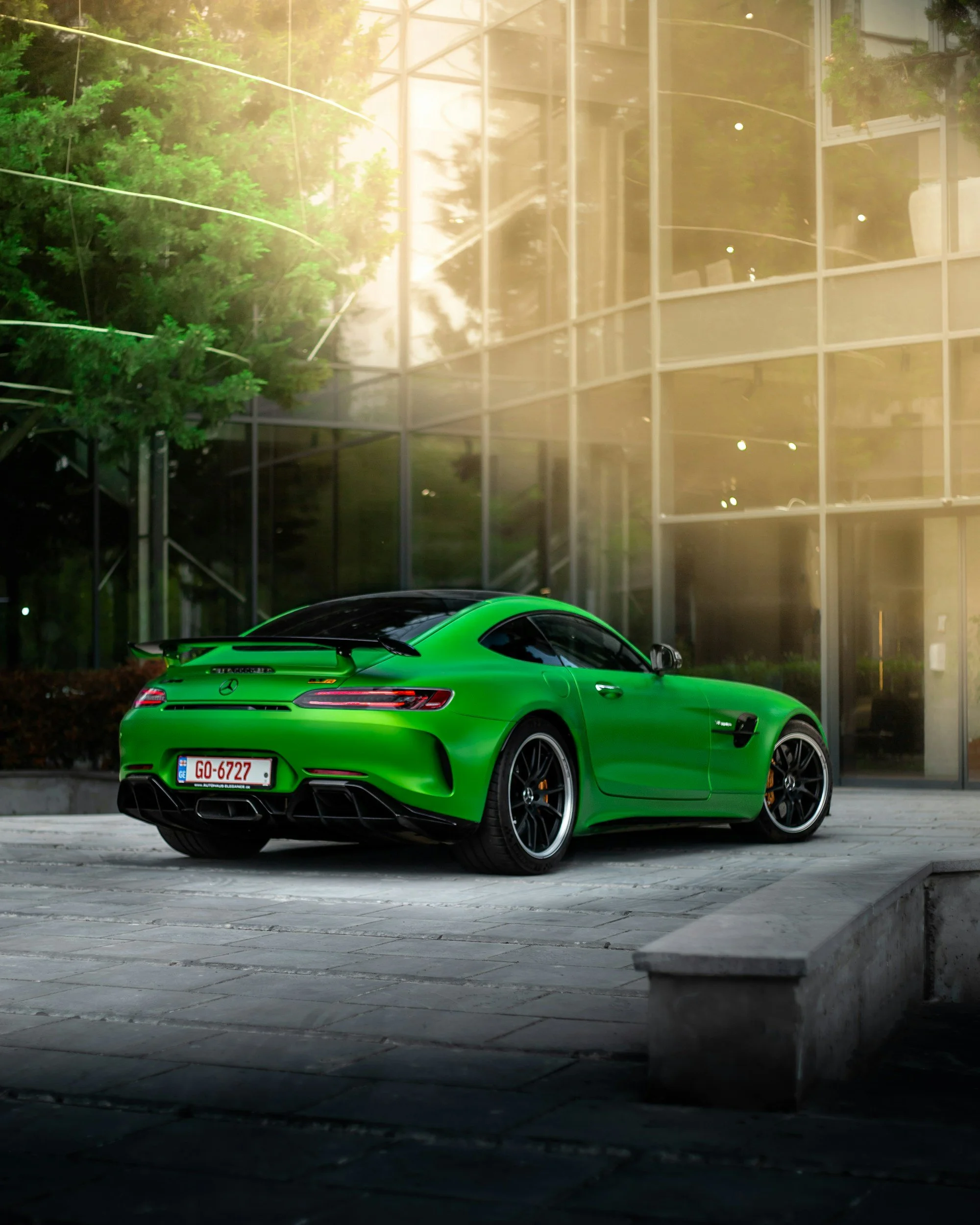 A bright green Mercedes-Benz sports car parked outside a modern glass building during golden hour sunlight.