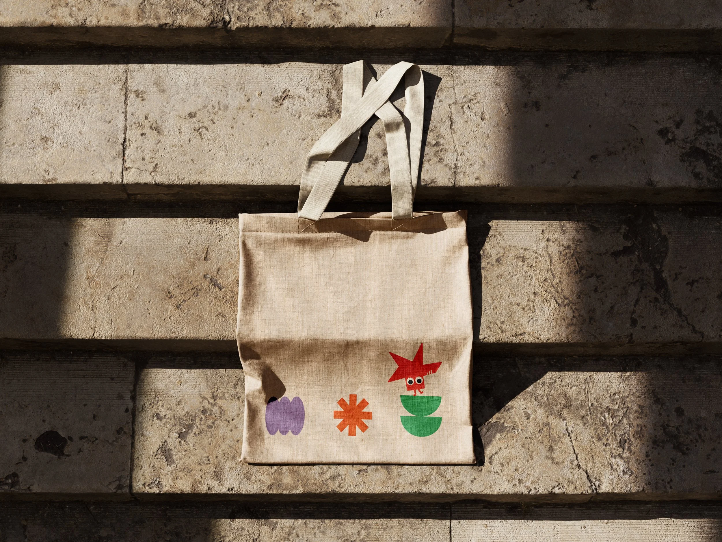 Een totebag met kleurrijke vormen en een rood mannetje met grote ogen.