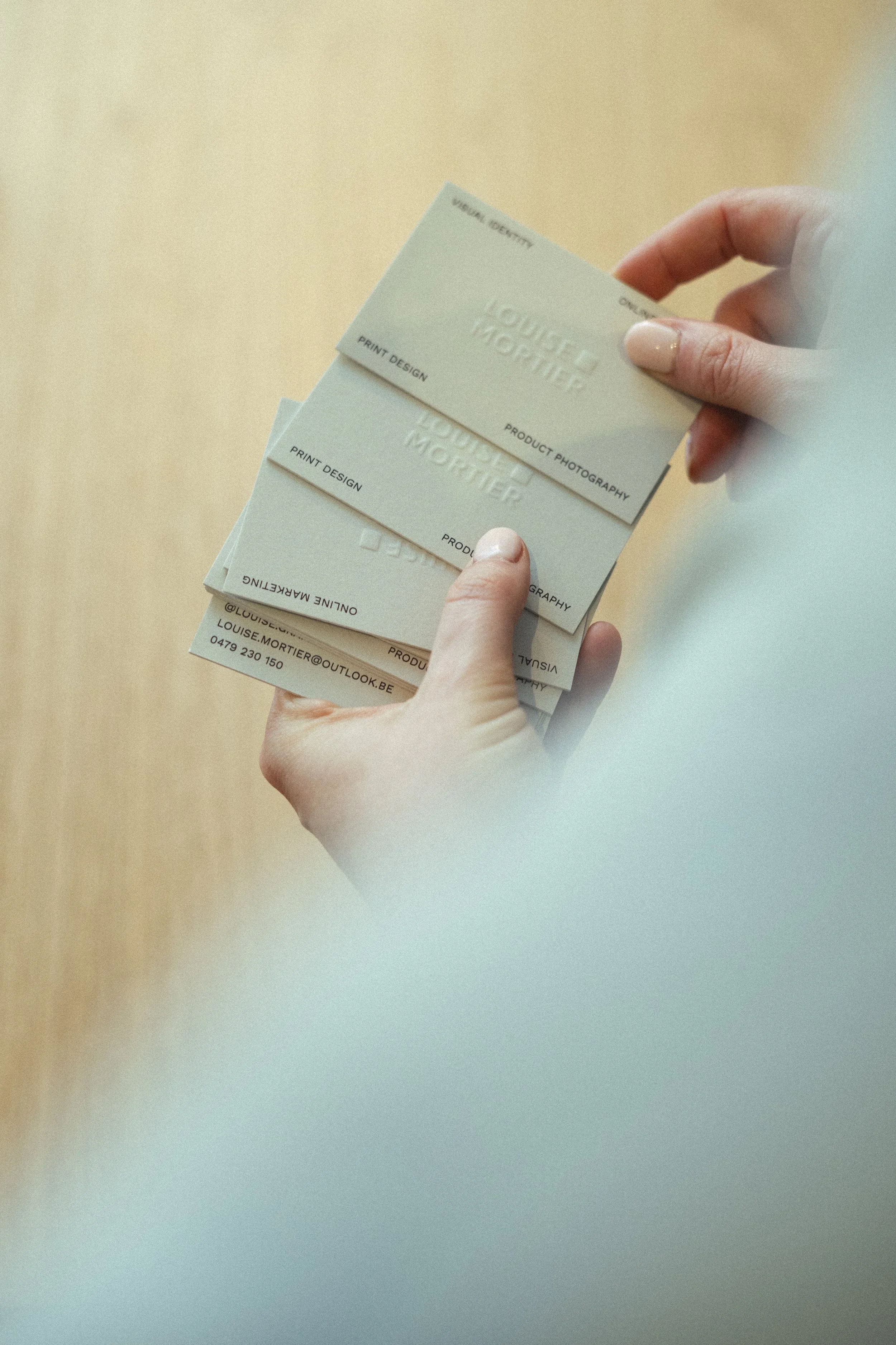 A person holding three business cards with contact information and design details.