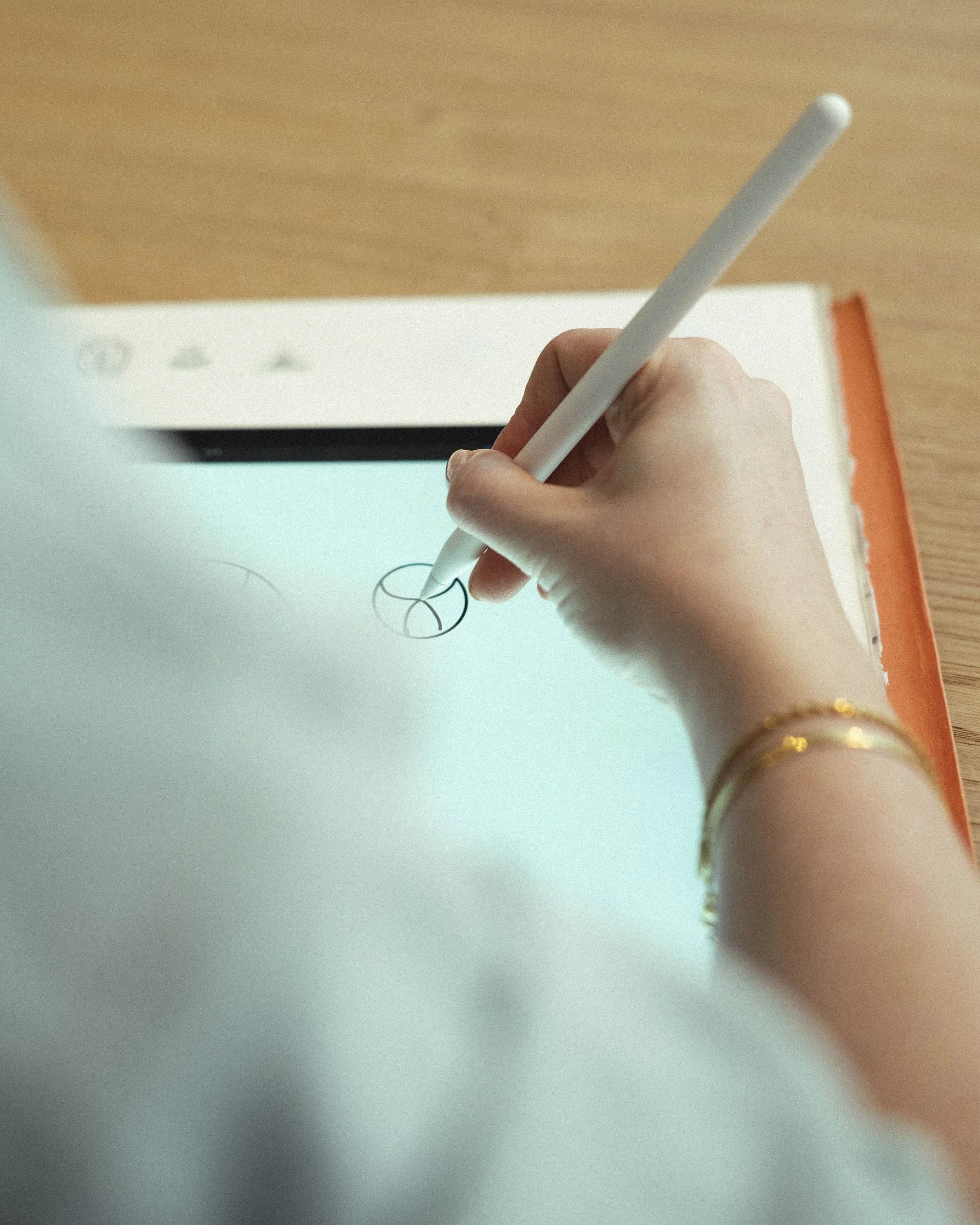 De afbeelding toont een hand die een pen vasthoudt en tekenen maakt in een open notitieboek op een houten tafel.