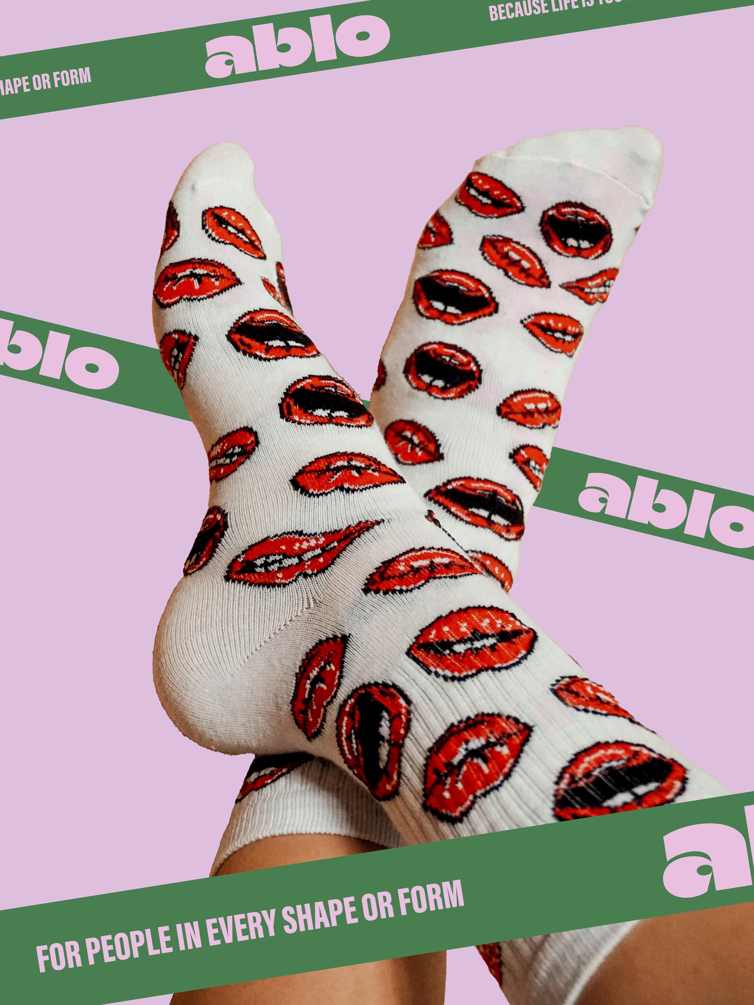 A pair of feet wearing white socks covered with a red lipstick kiss pattern, positioned against a lavender background with green and pink text and design elements.