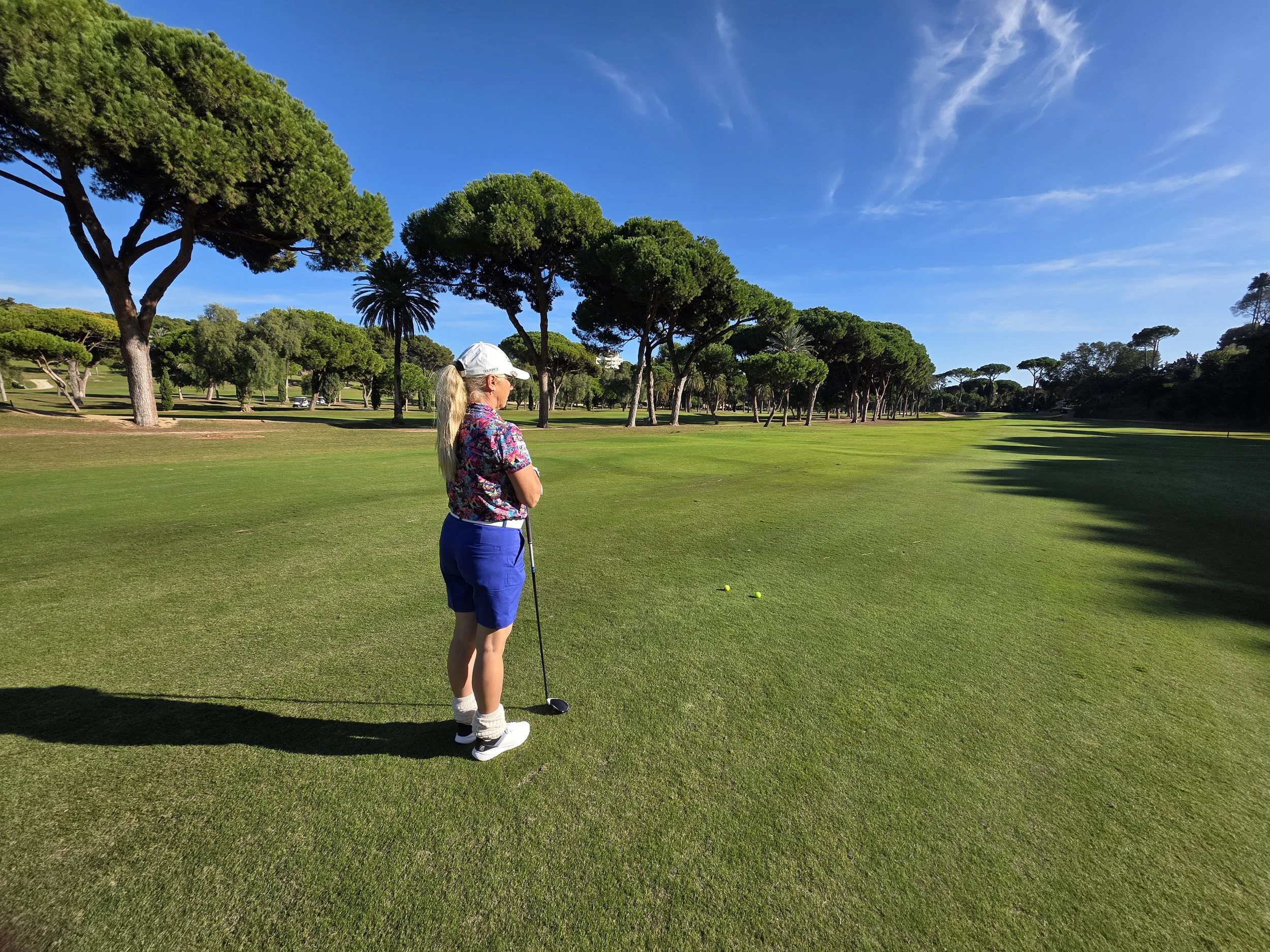 Golfschülerin blickt auf den Golfplatz La Cala mit Pinien im Hintergrund
