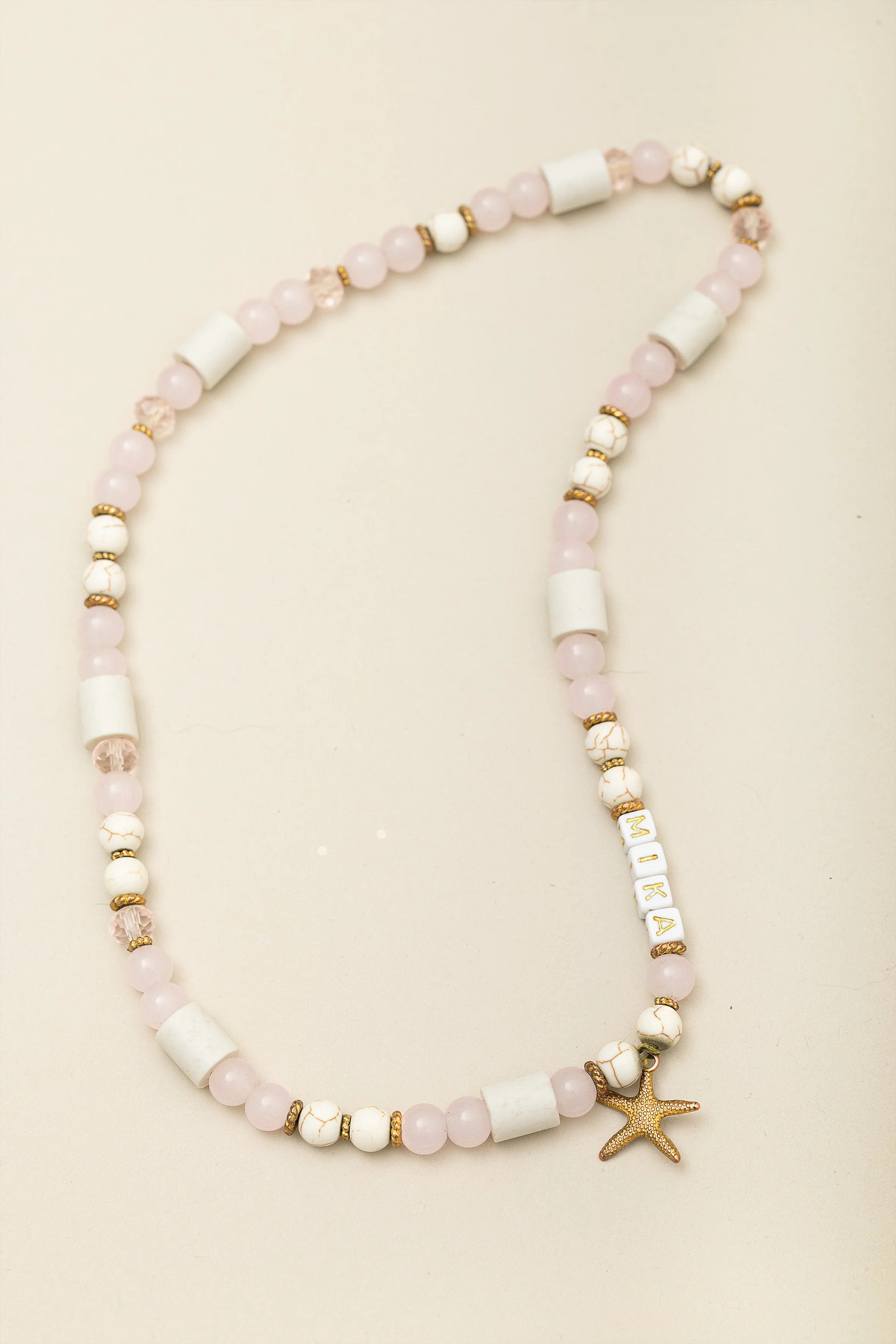 Perlenkette in rosa, weiß und gold mit einem kleinen goldfarbenen Sternanhänger und namens Buchstaben
