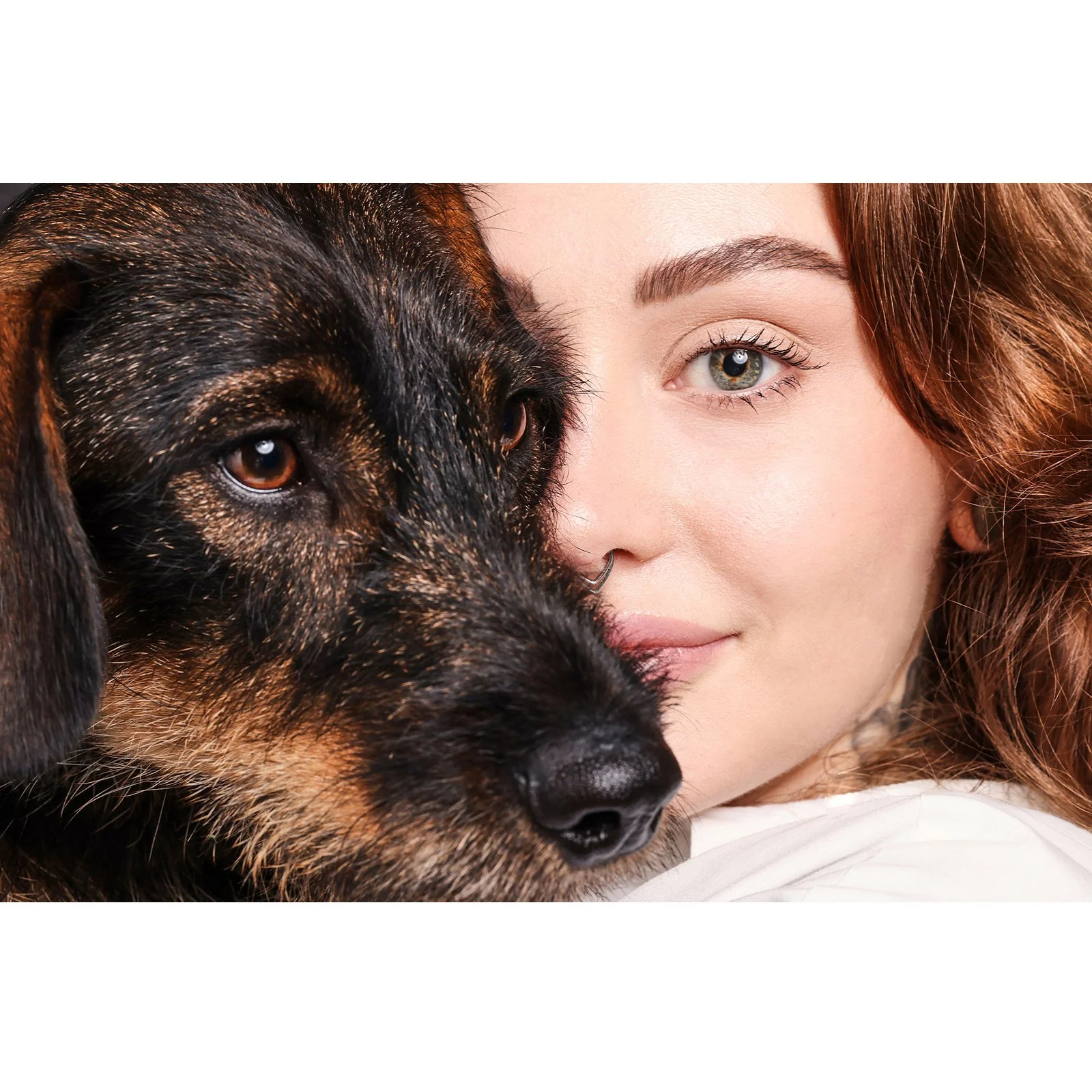 Junge Frau mit roten Haaren hält ein Hund vor ihrem Gesicht, beide Blick in die Kamera