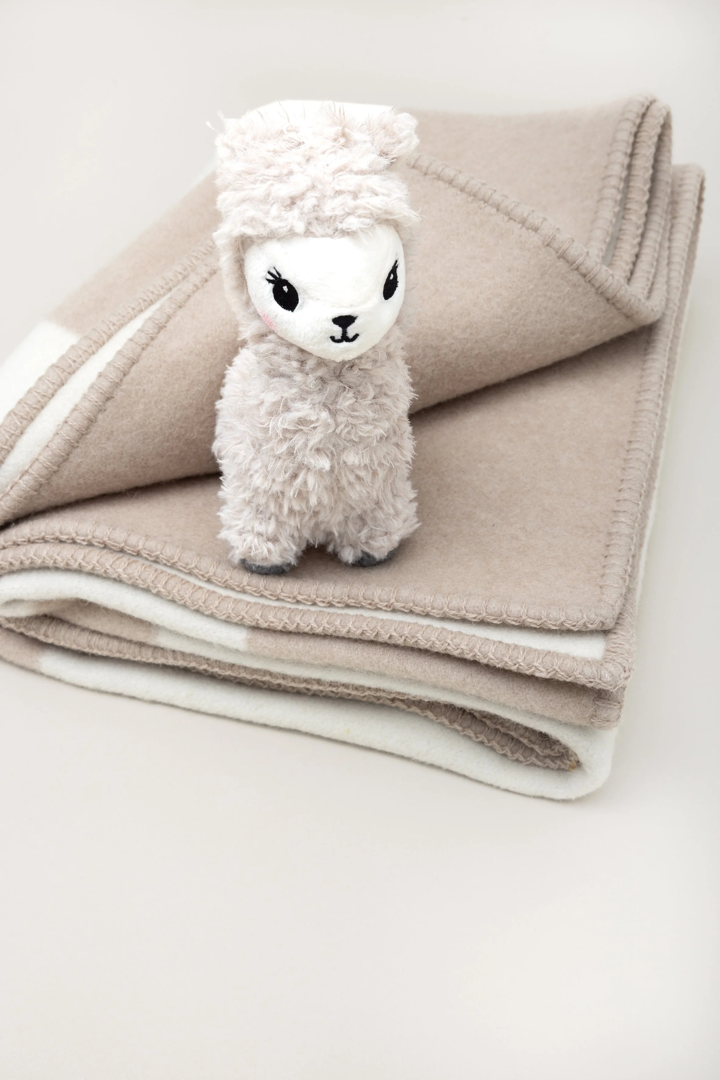 Ein Plüschtier in Form eines Lamas steht auf einem beige gefärbten Wollteppich, der auf einer weißen Oberfläche liegt.