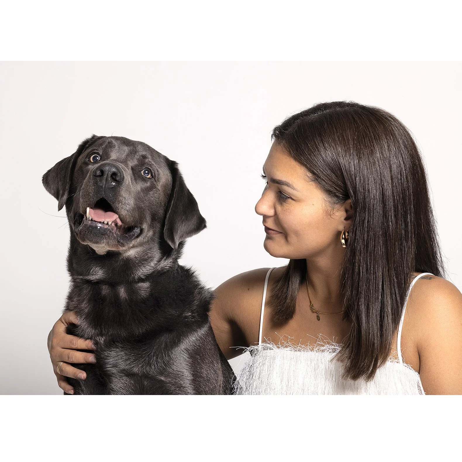 Eine Frau hält einen schwarzen Hund, der freundlich aussieht, vor weißem Hintergrund. Sie blickt ihn liebevoll an.