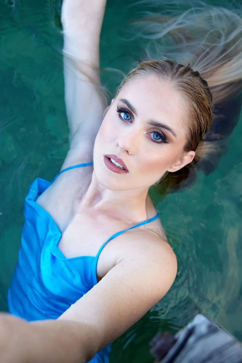 Ein schöne Frau mit blauen Augen trägt ein blaues Kleid und liegt im Wasser, wobei sie ein Selfie macht.