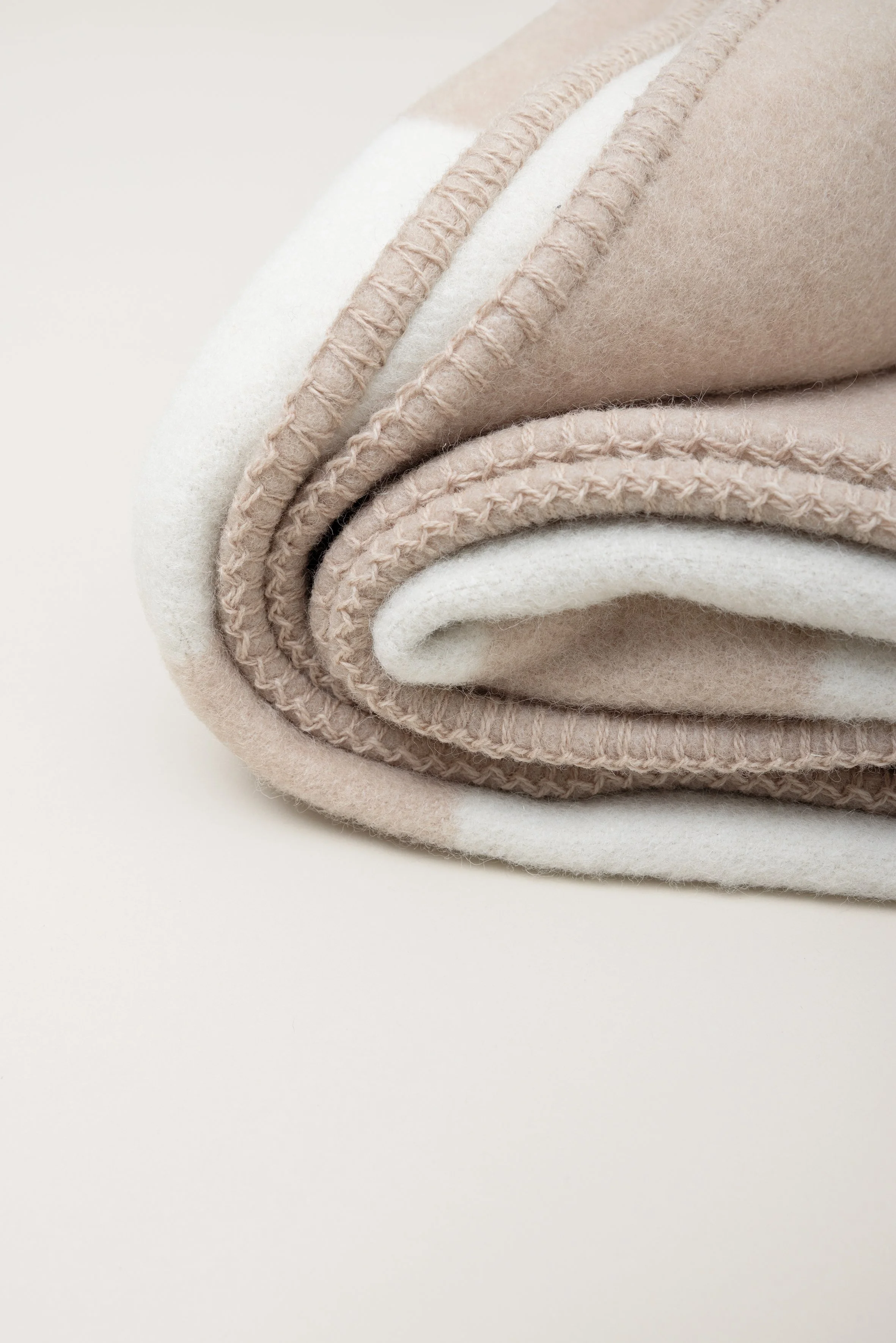 Nahaufnahme eines einrollten, zweilagigen Bettlakens oder Decken, beige und cremefarben, mit gesticktem Rand, aus weichem Stoff.