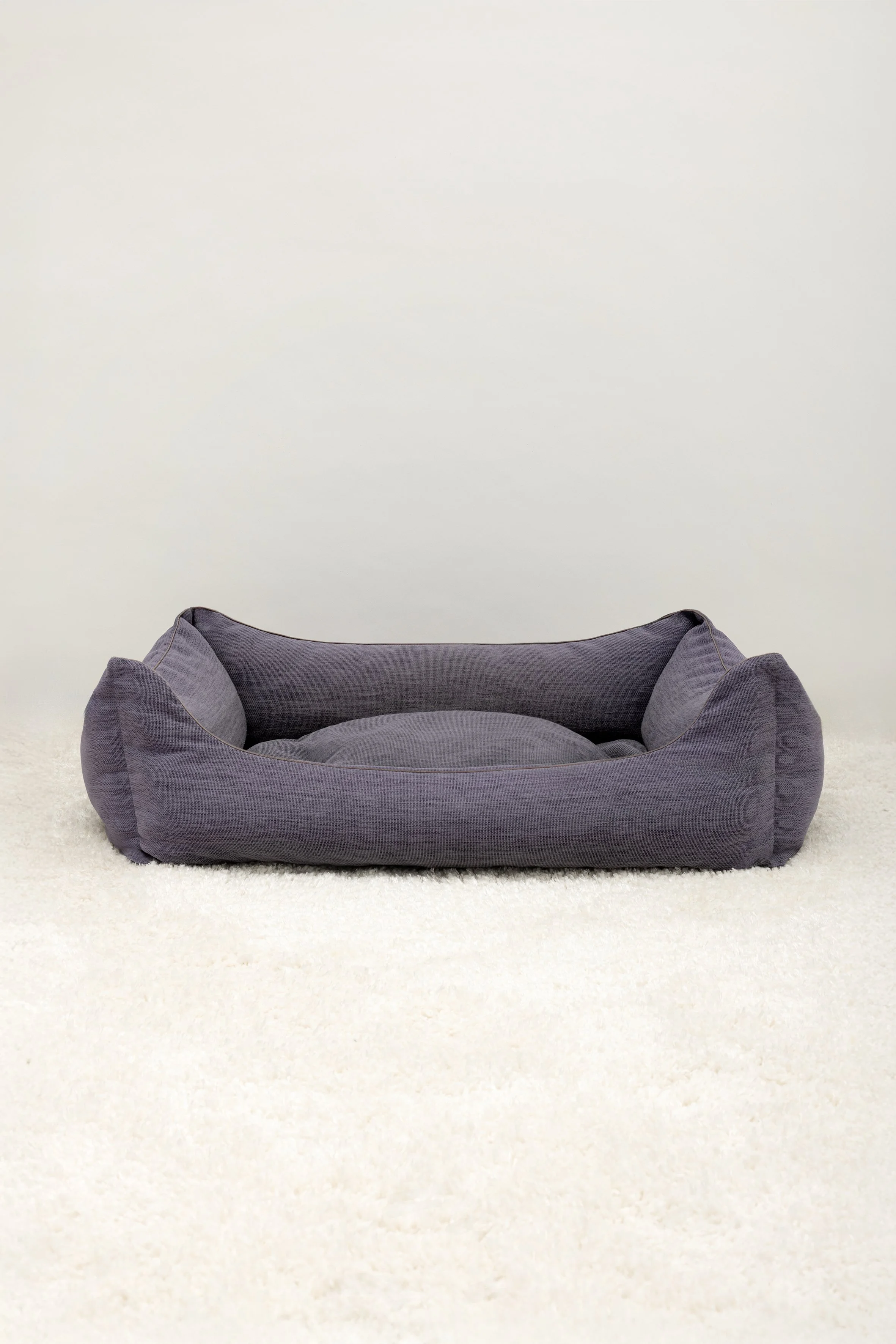 Ein graues Kuschelsofa auf einem weißen Teppich vor einer weißen Wand.