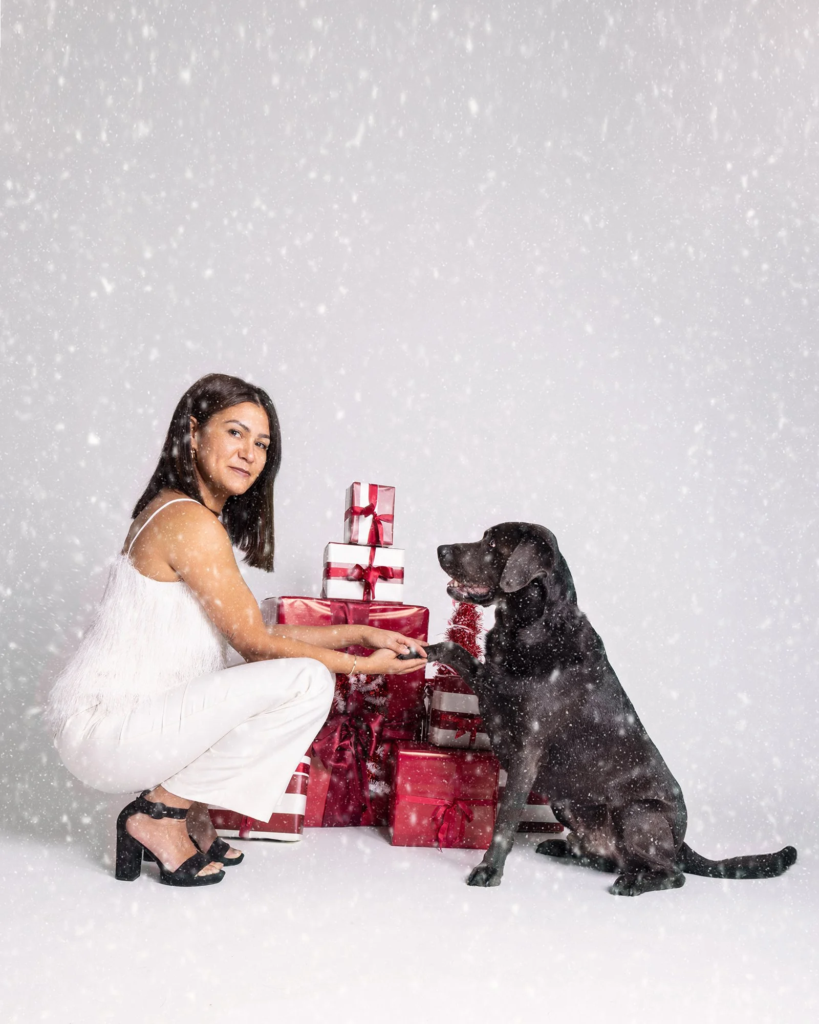 Frau und Hund mit Weihnachtsgeschenken im Schneefall, festliche Stimmung.