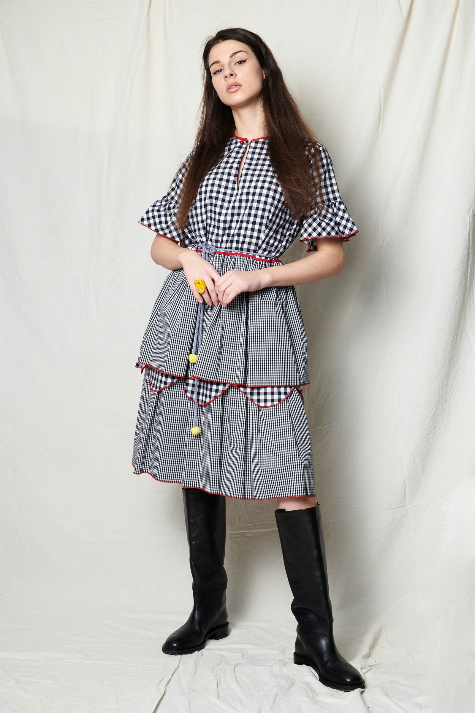 Eine junge Frau mit langem braunem Haar trägt ein schwarzes und weiß kariertes Kleid mit roten Nähten, kombiniert mit hohen schwarzen Stiefeln.
