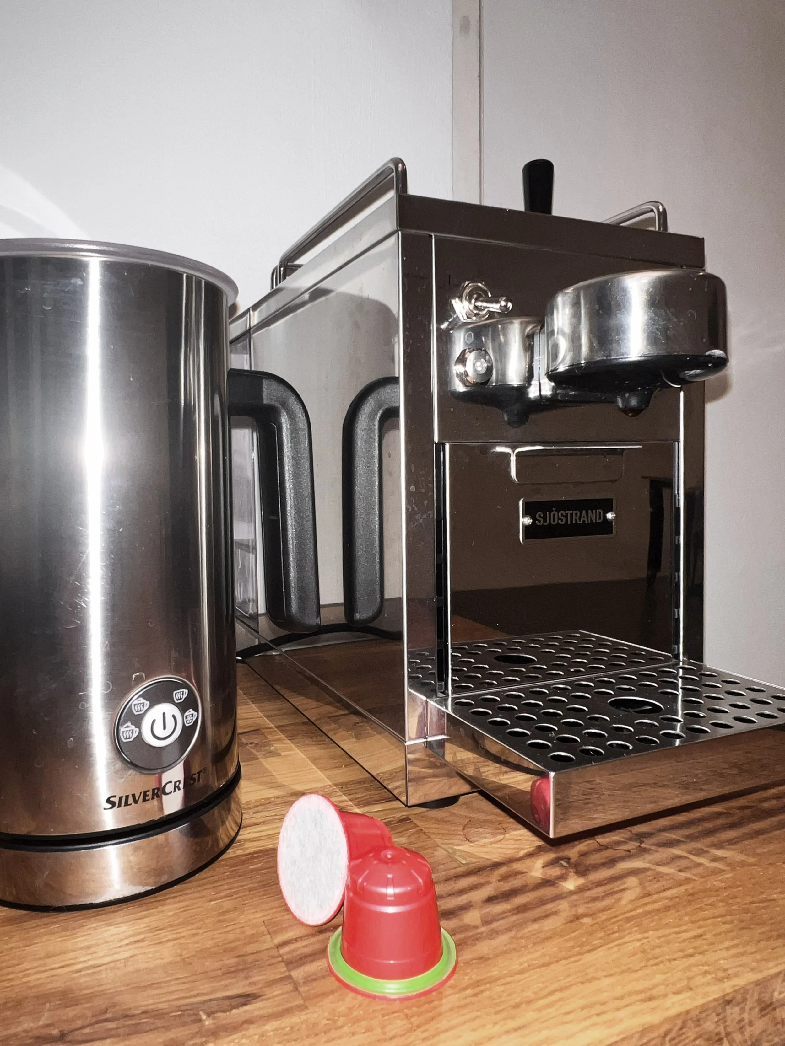 Kaffeemaschine und Wasserkocher auf einem Holztisch mit einem roten Kaffeekapsel auf dem Tisch.