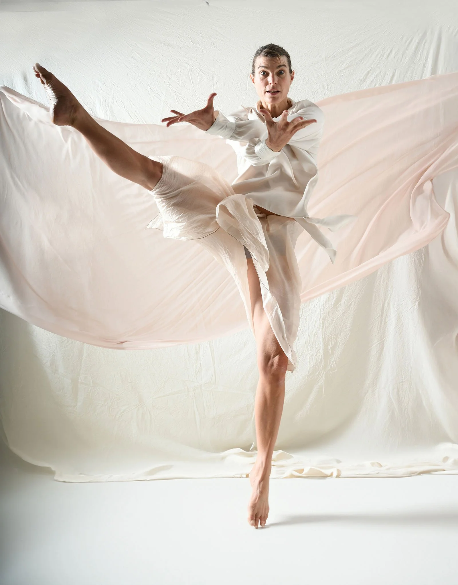 Eine tanzende Person in einem weißen Kleid vor einem weißen Hintergrund.