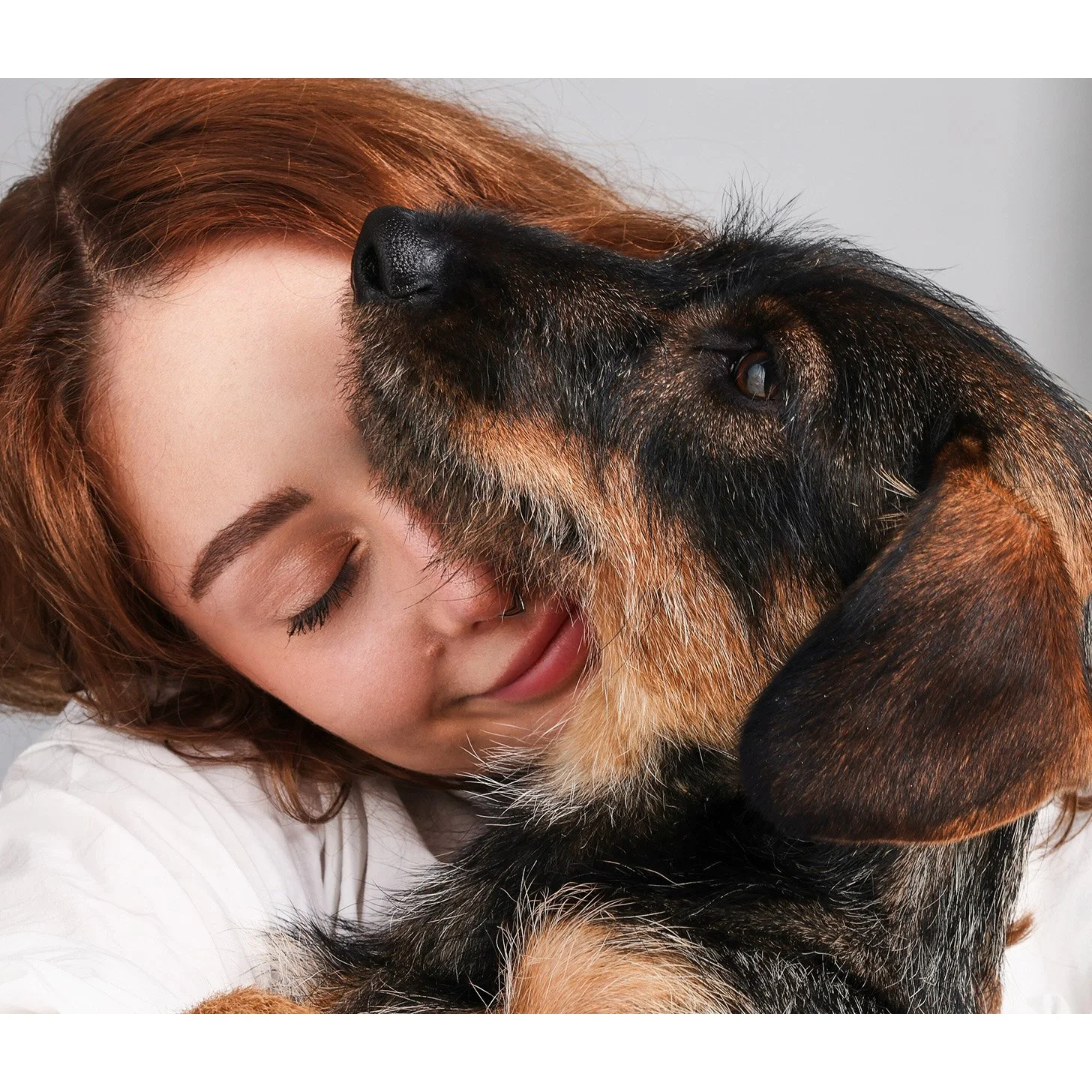 Eine junge Frau mit geschlossenen Augen umarmt einen Hund, der an ihr schnüffelt.
