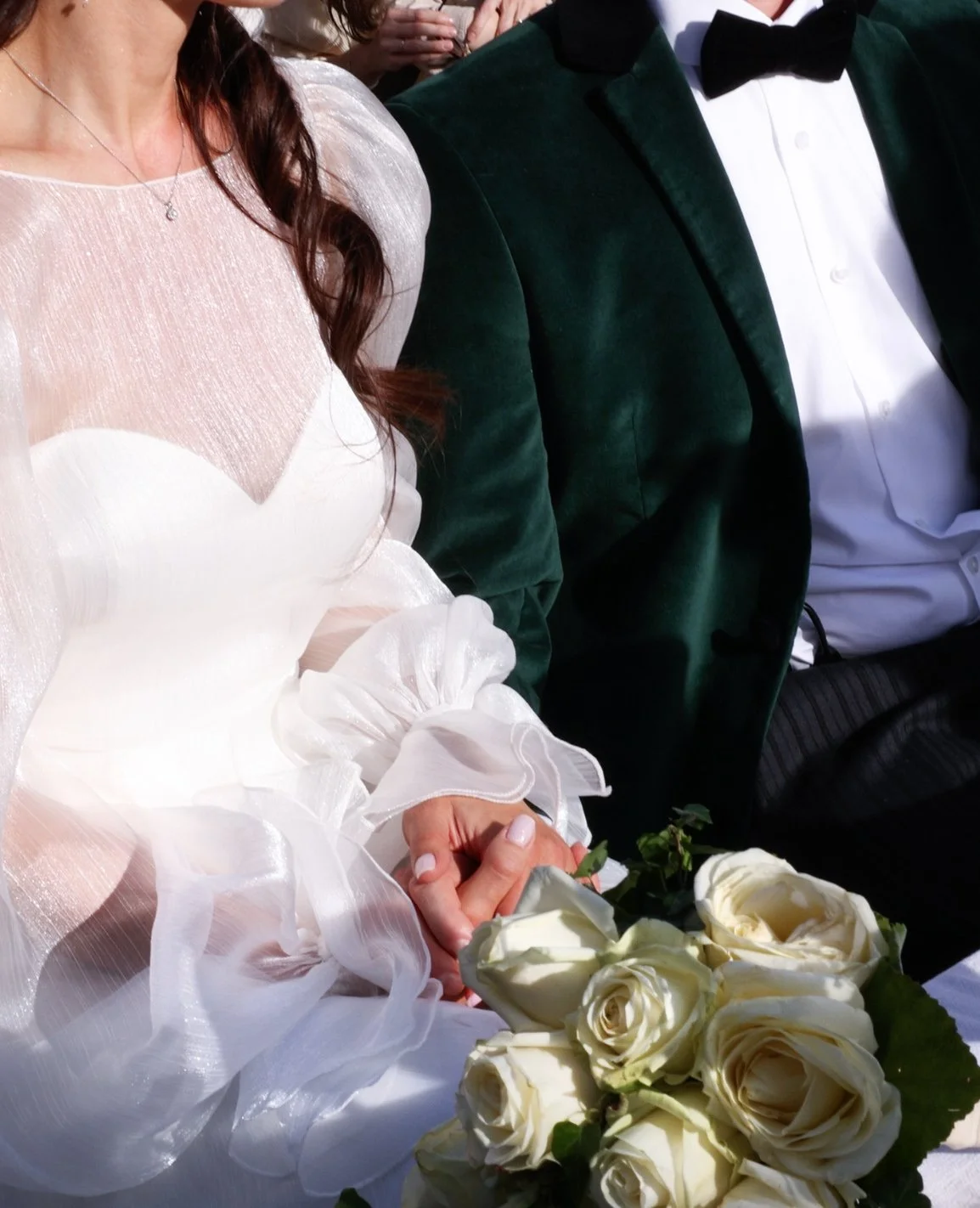 Hochzeitspaar in festlicher Kleidung hält weiße Rosen bei einer besonderen Zeremonie.