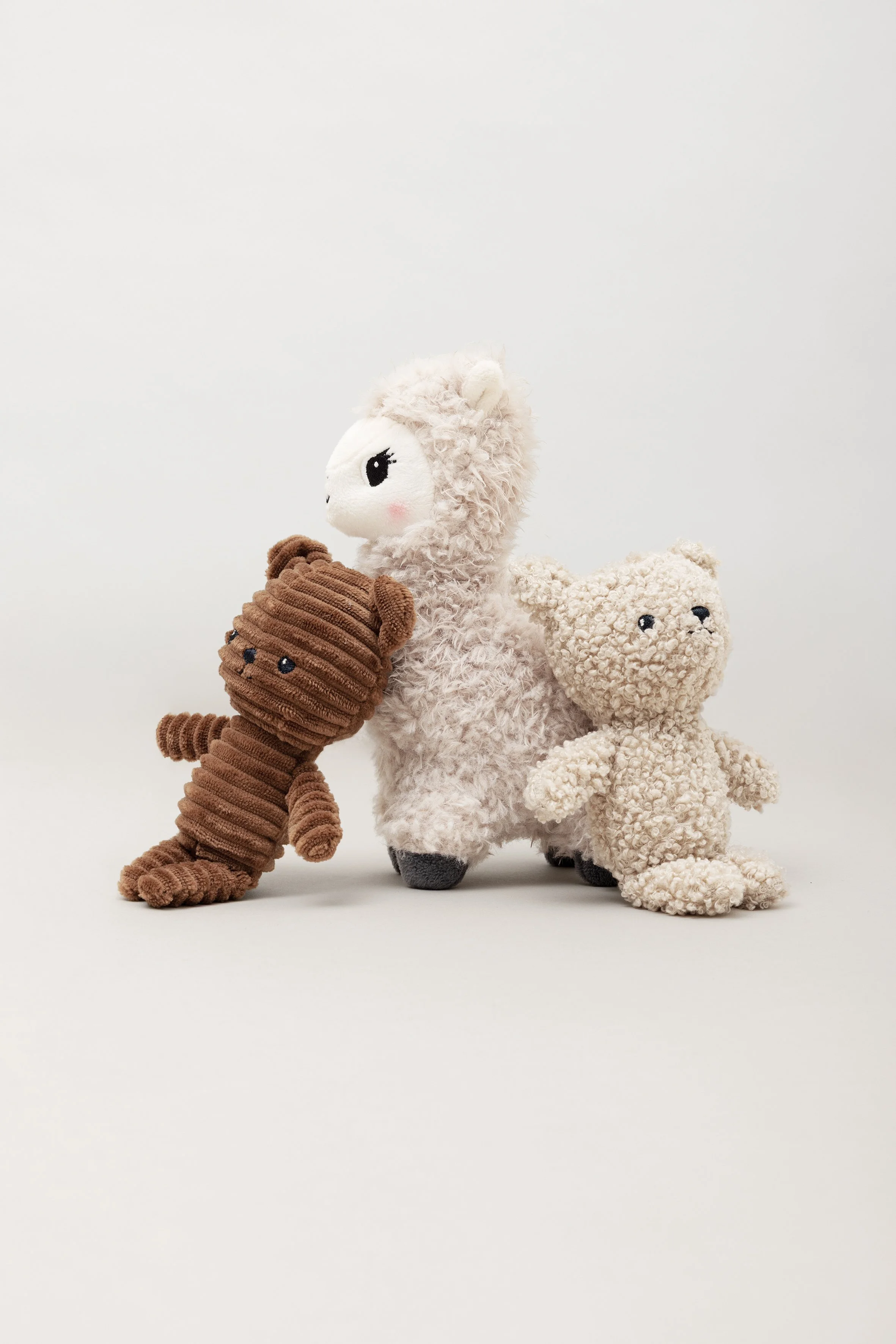 Vier Plüschtiere: Ein braunes, plüschiges Krokodil, eine weiße Lama, eine braune, wollige Eule und ein beige Teddybär vor einem weißen Hintergrund.