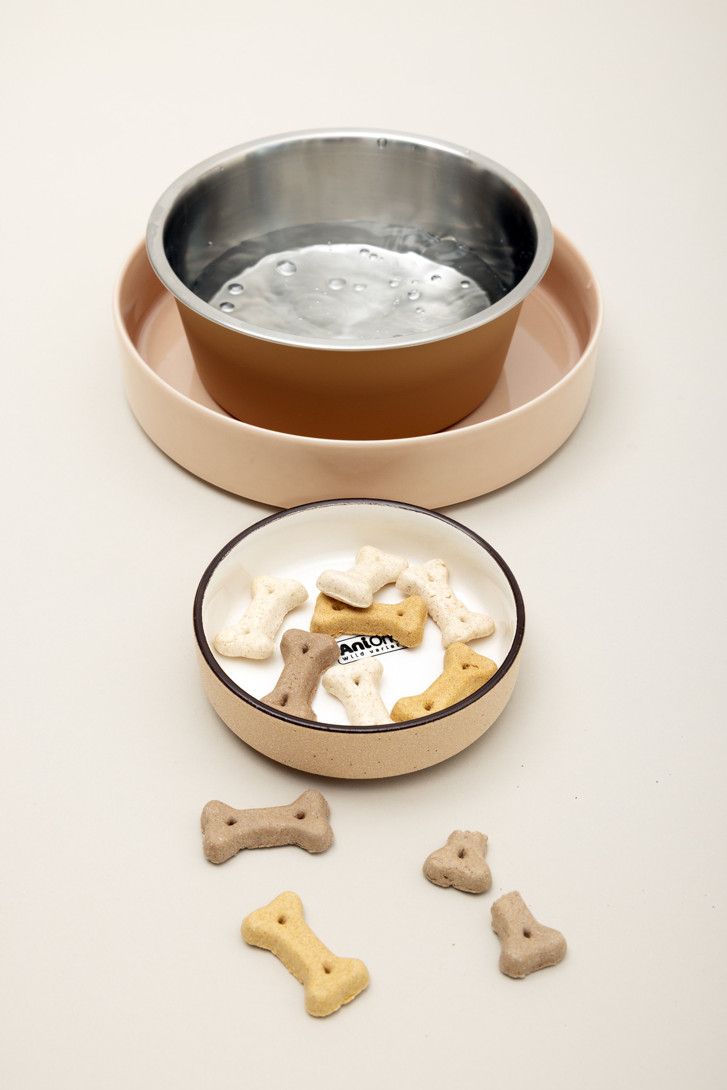 Zwei Schalen, eine mit Wasser und die andere mit Hundekeksen in Form von Knochen, auf einem weißen Tisch.