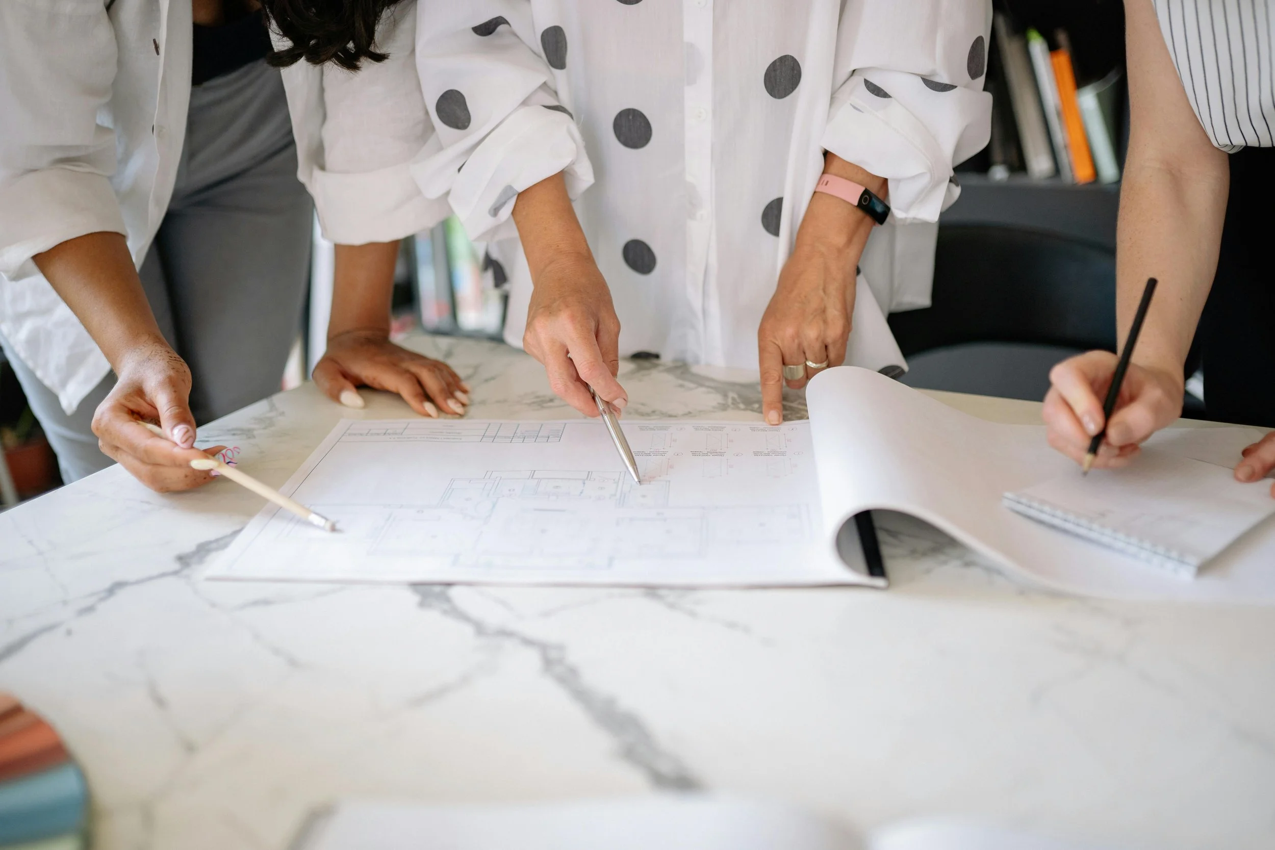 Three people examining architectural blueprints on a marble table.
