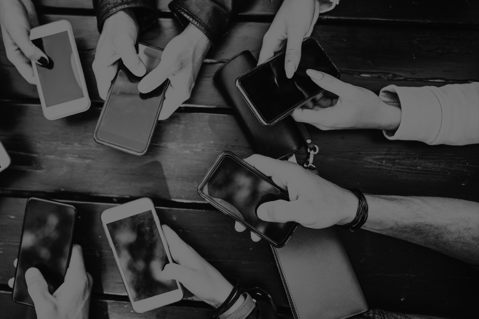 Several people sitting around a wooden table using their smartphones.