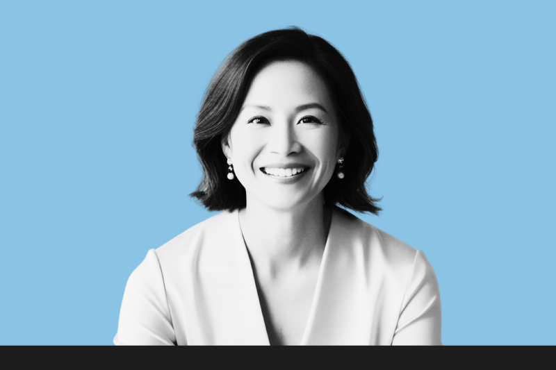 A smiling woman with shoulder-length dark hair, wearing pearl earrings and a light-colored top, against a light blue background.