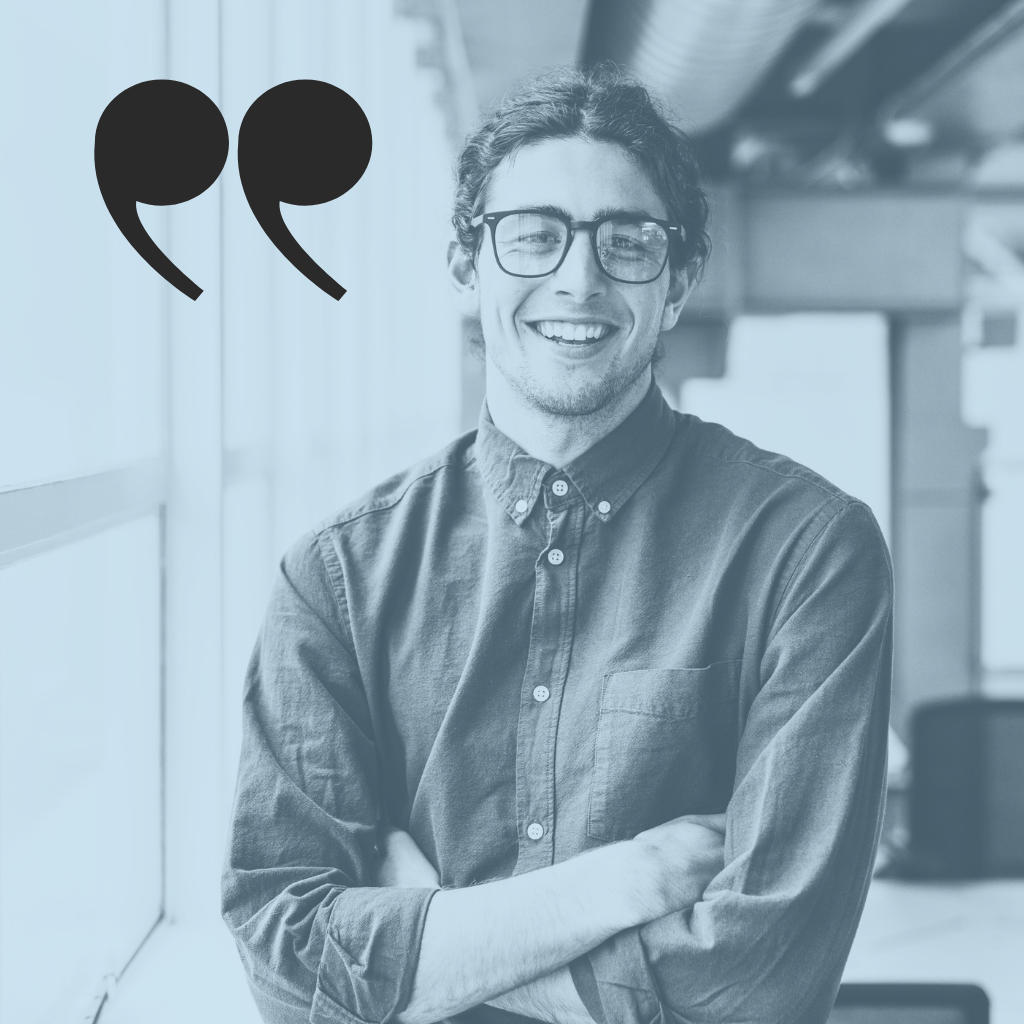 A young man with glasses, smiling, standing with arms crossed in an indoor setting with a quote mark graphic beside him.
