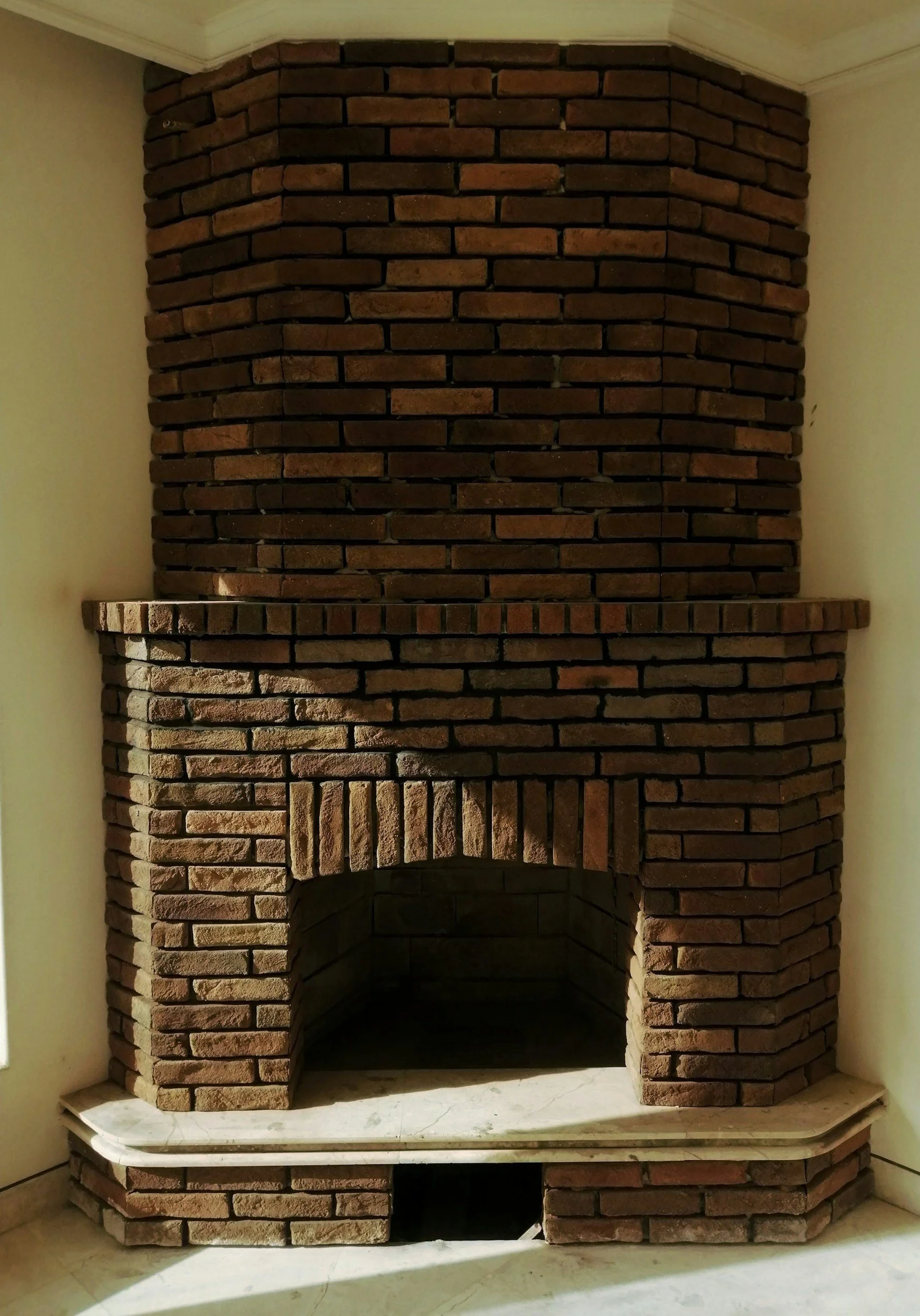 Brick fireplace with a marble mantel and a rounded top, located in a corner of a room.