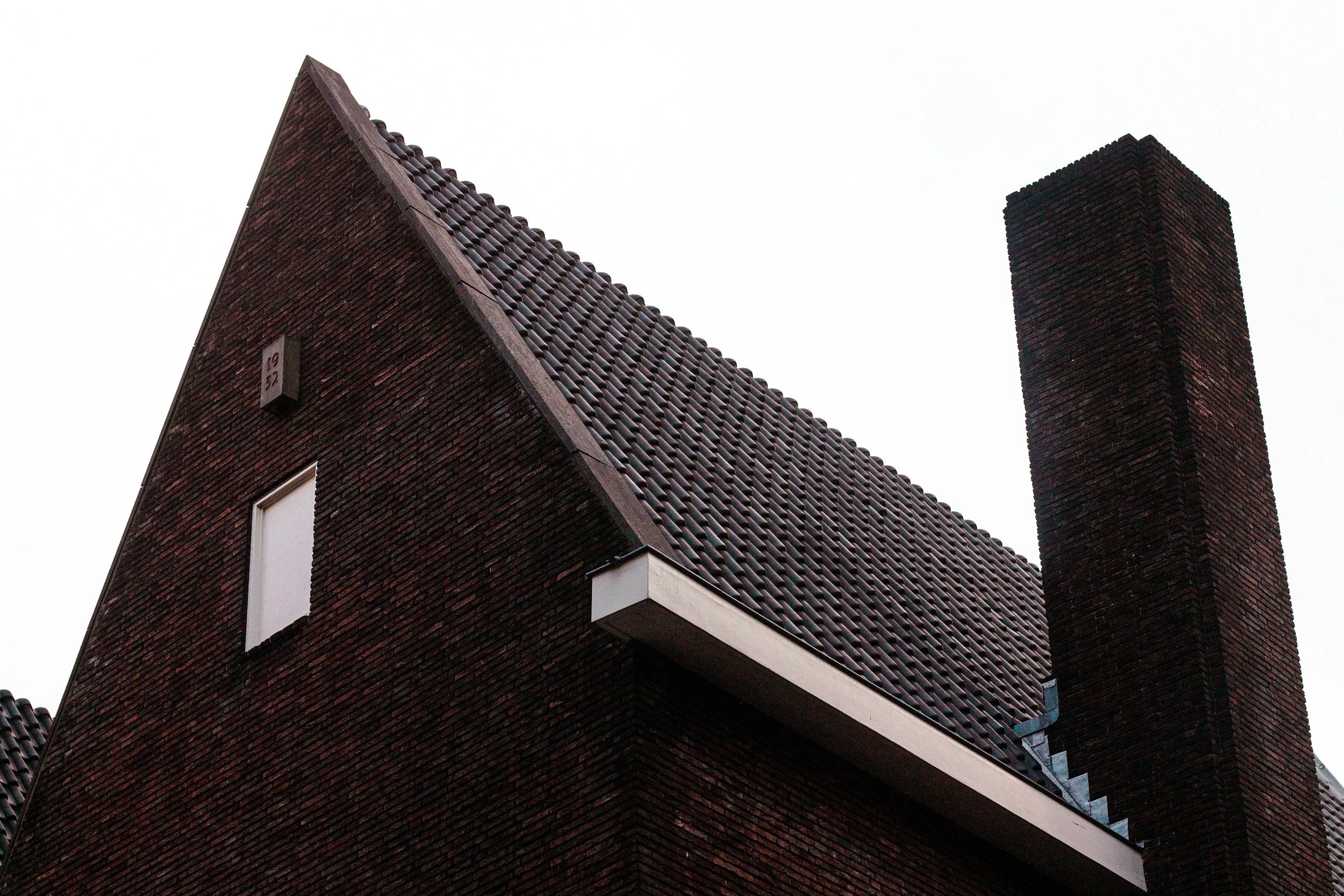 Close-up of a modern brick house with a sloped roof and an attached chimney, with the sky in the background.