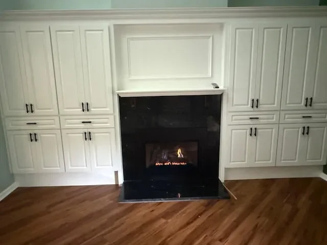 Fireplace with black surround in a room with white cabinets and wood flooring.