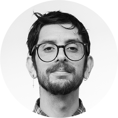 Retrato en blanco y negro de un hombre joven con gafas, barba y earring, sonriendo ligeramente.