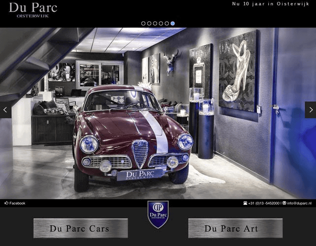 Een klassieke rode auto met witte rijstrook op een autoshowroom, omgeven door kunstwerken en informatieschermen.