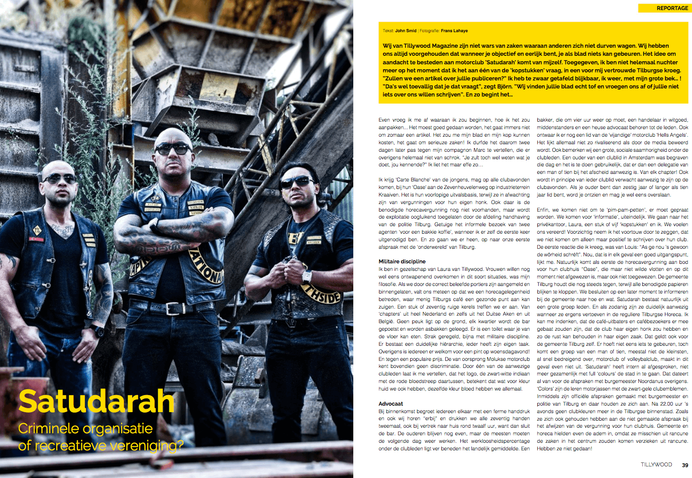 Drie mannen in zwarte cluboutfits en zonnebrillen staan voor een roestige, industrieel ogende achtergrond met trappen en planten.