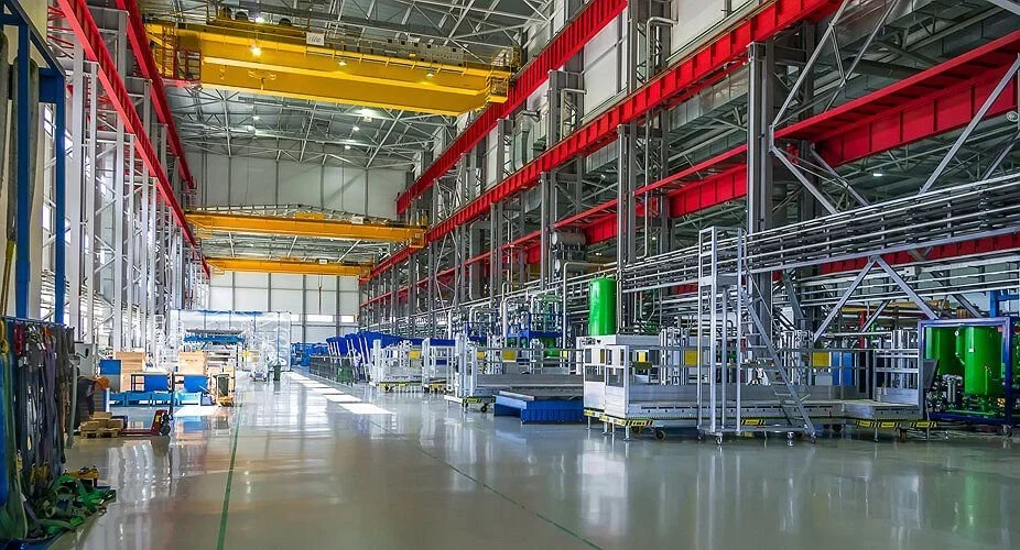 Interne view van een grote industriële fabriekshal met verschillende machines, transportbanden en een hijskraan.