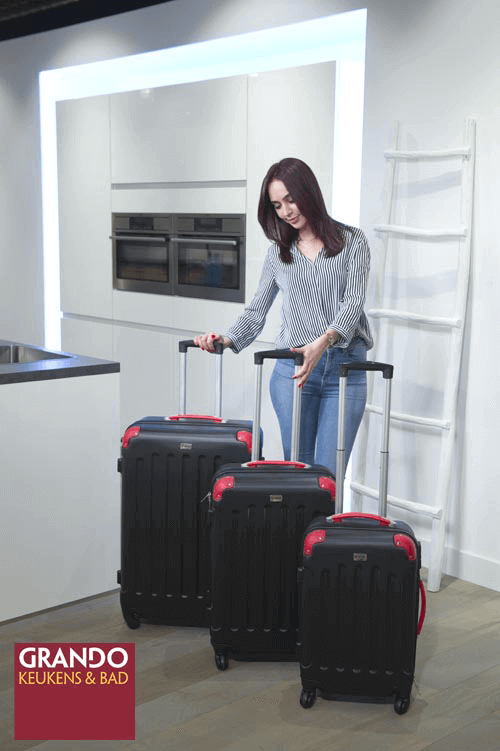 Vrouw met drie zwarte koffers met rode details in een moderne keuken.