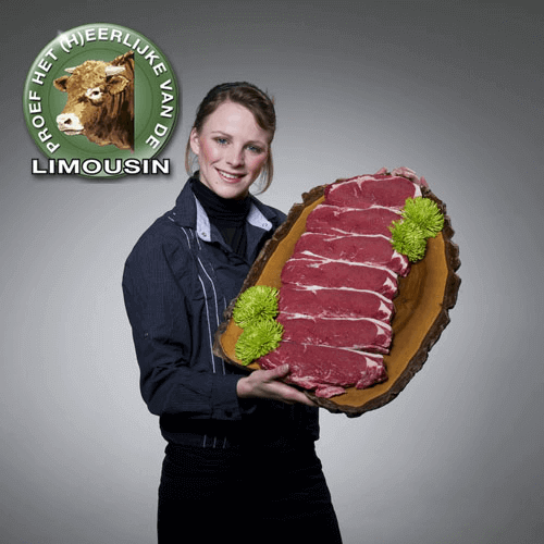 Vrouw houdt een groot bord met plakken rood vlees en groene decoraties, met een logo van een koe en de tekst 'Het Heerlijke Van De Limousin'.
