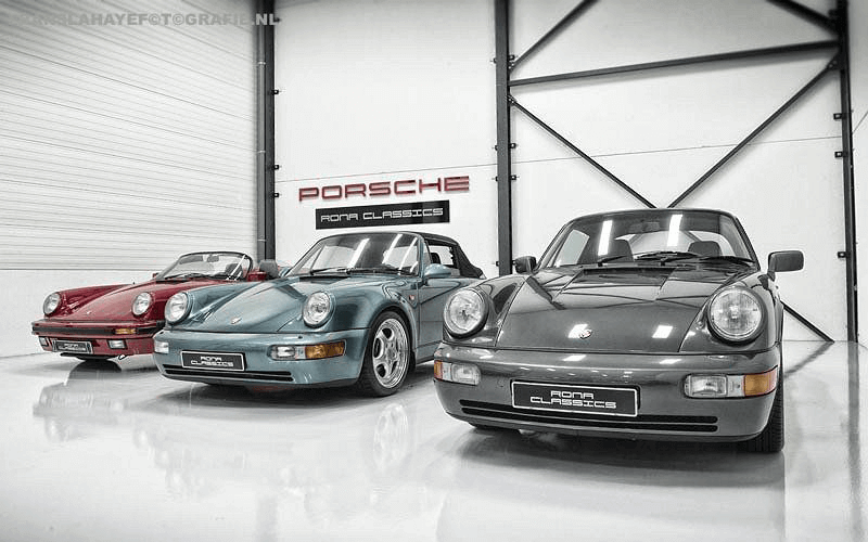 Drie Porsche 911 sportwagen in een verzamelruimte met witte muren en een deur met een Porsche Rona Classics bord.