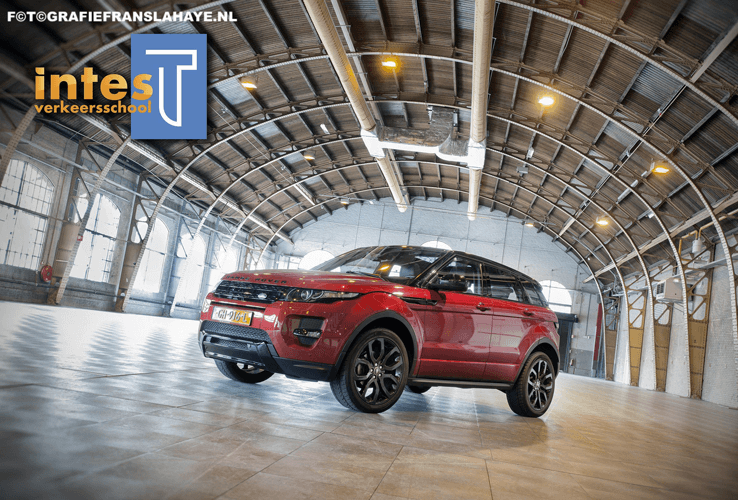 Een rode Range Rover Evoque in een indoor rijschoolomgeving met een houten plafond en grote ramen.